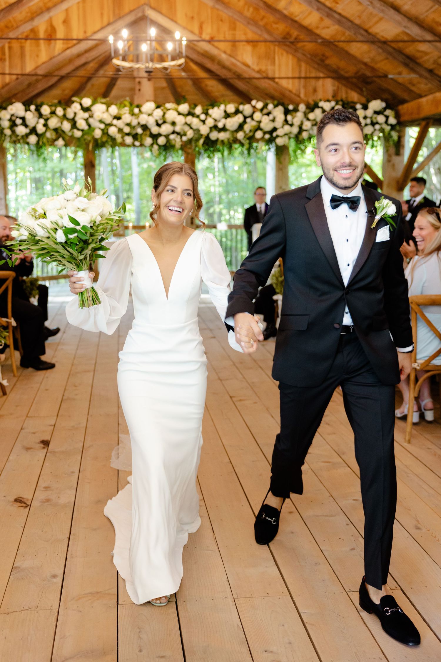 Wedding celebration in an elegant wooden pavilion with chandelier and floral decorations.