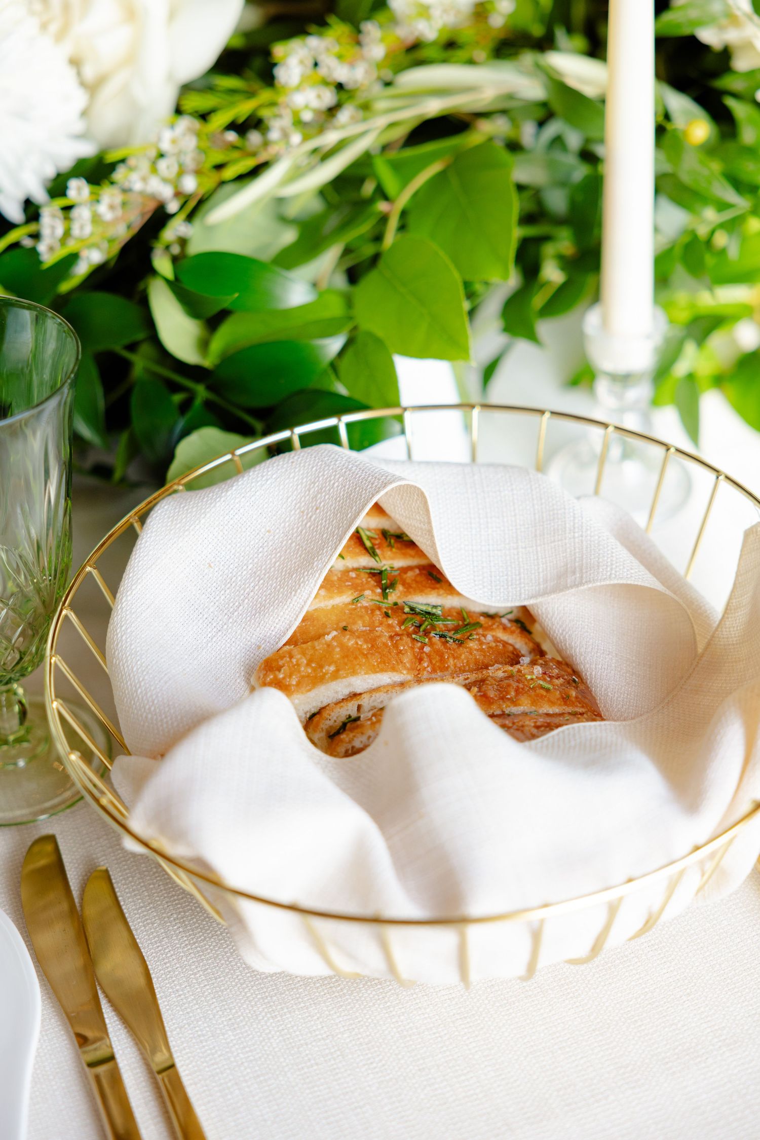 Gold-rimmed basket with white napkin and bread served at an elegant table setting.