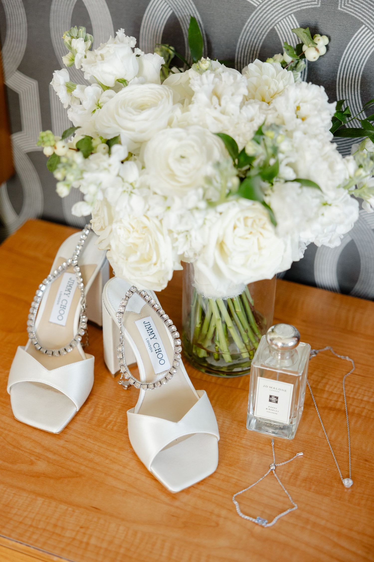 White bridal shoes and roses arranged with perfume bottle on wooden surface.
