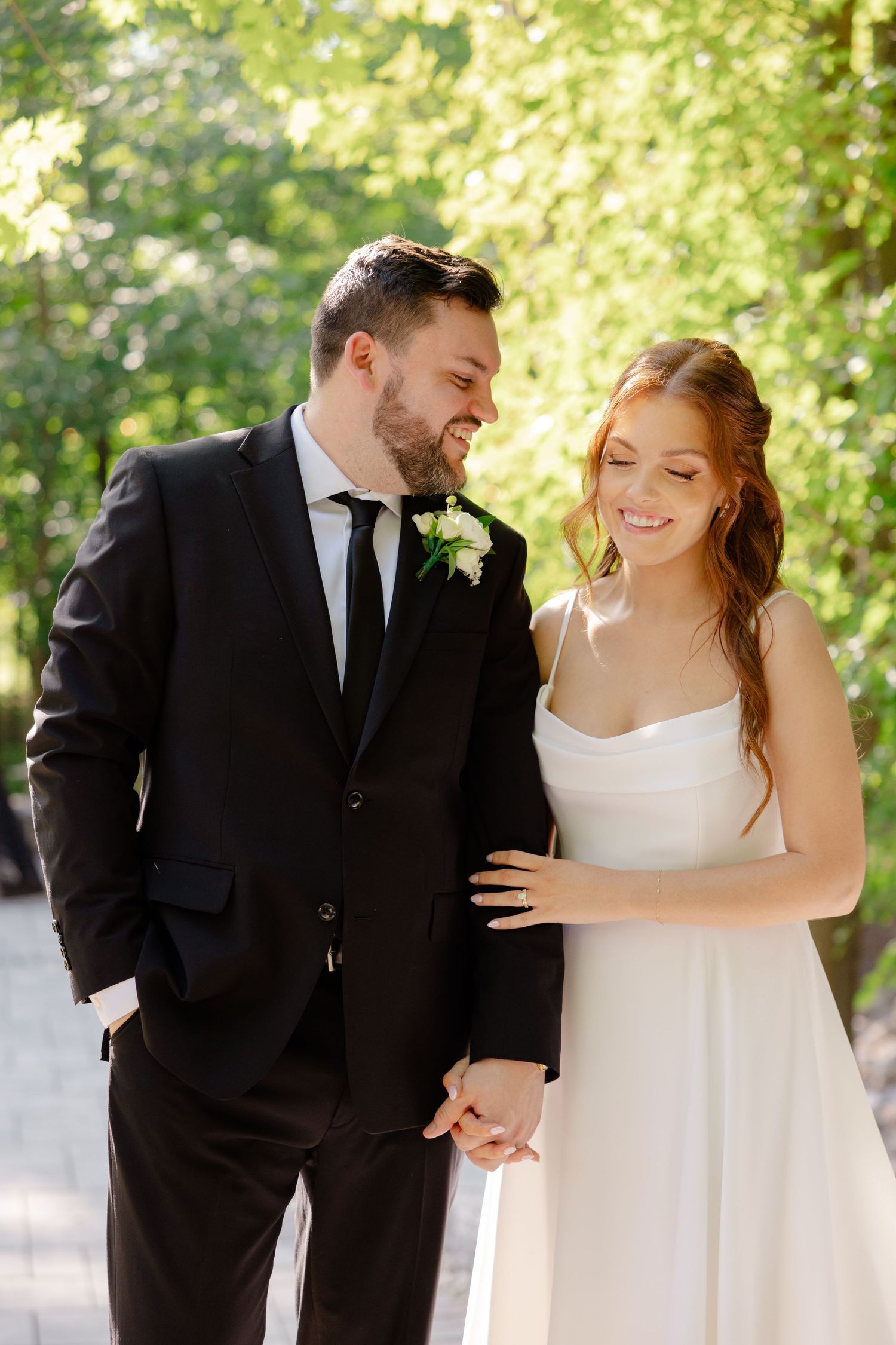 A candid wedding photo of a couple laughing together in bright natural sunlight.