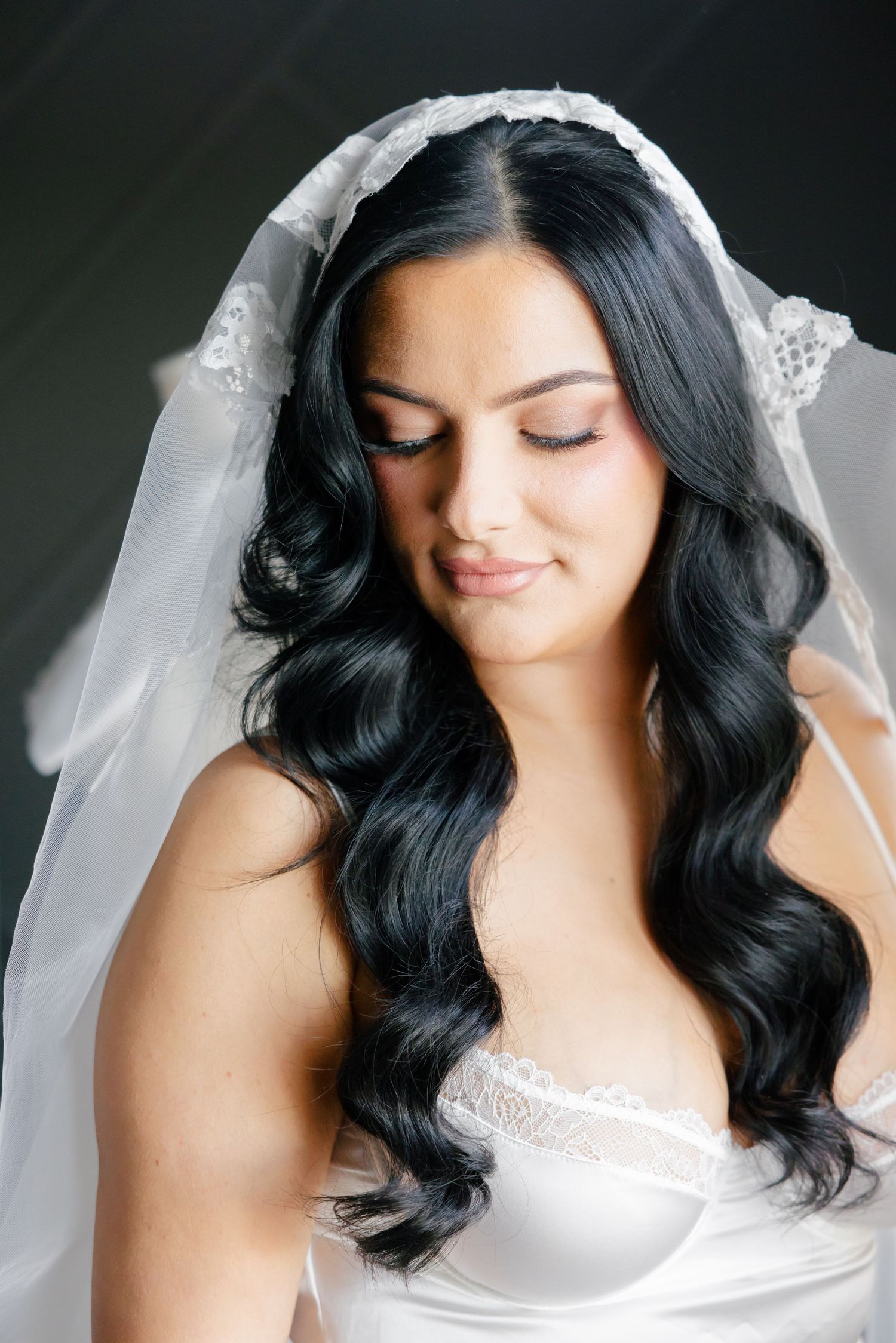 Close-up bridal portrait showing elegant dark wavy hair and delicate white veil.