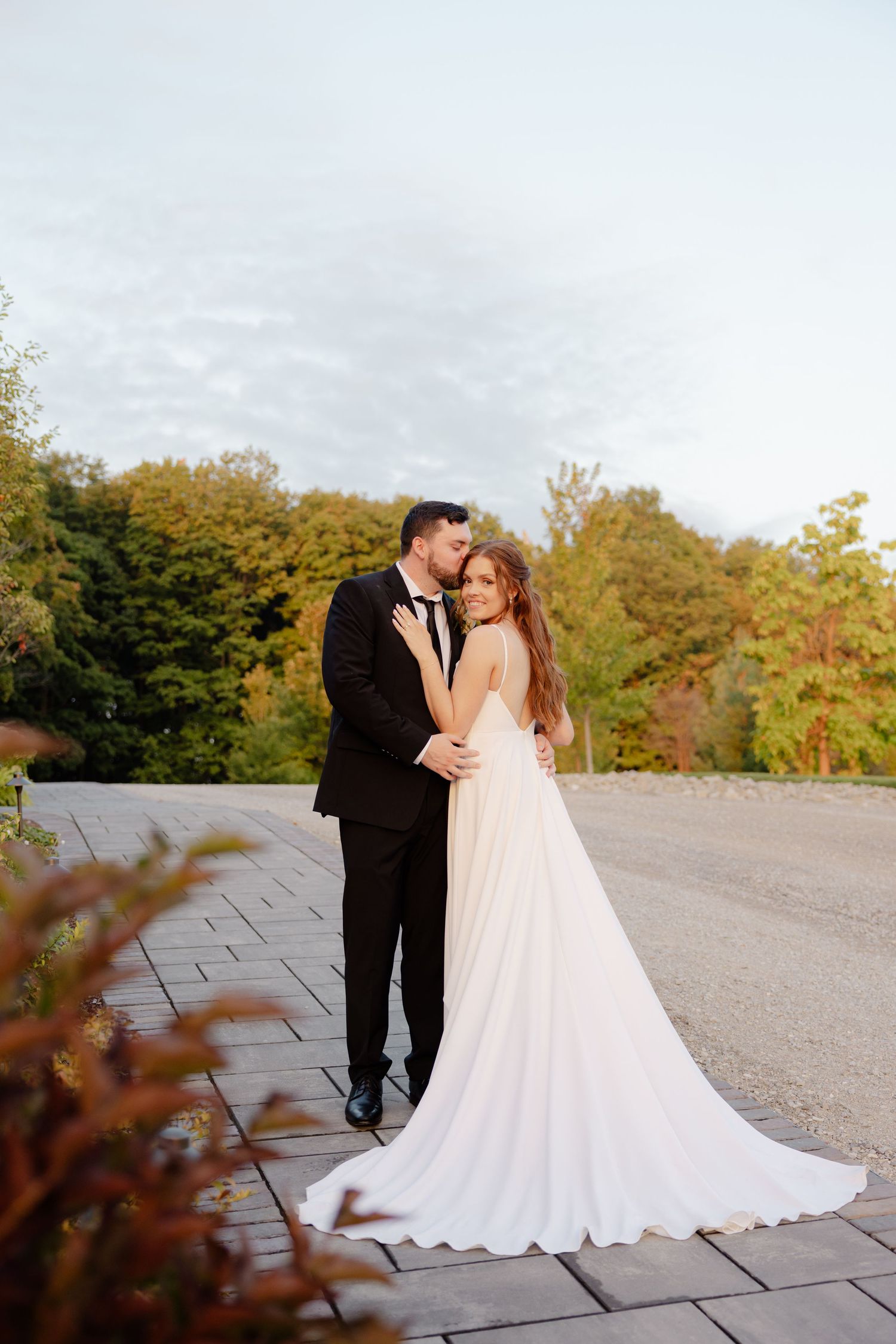 Autumn wedding portrait featuring a couple in elegant attire on a stone path surrounded by fall foliage.