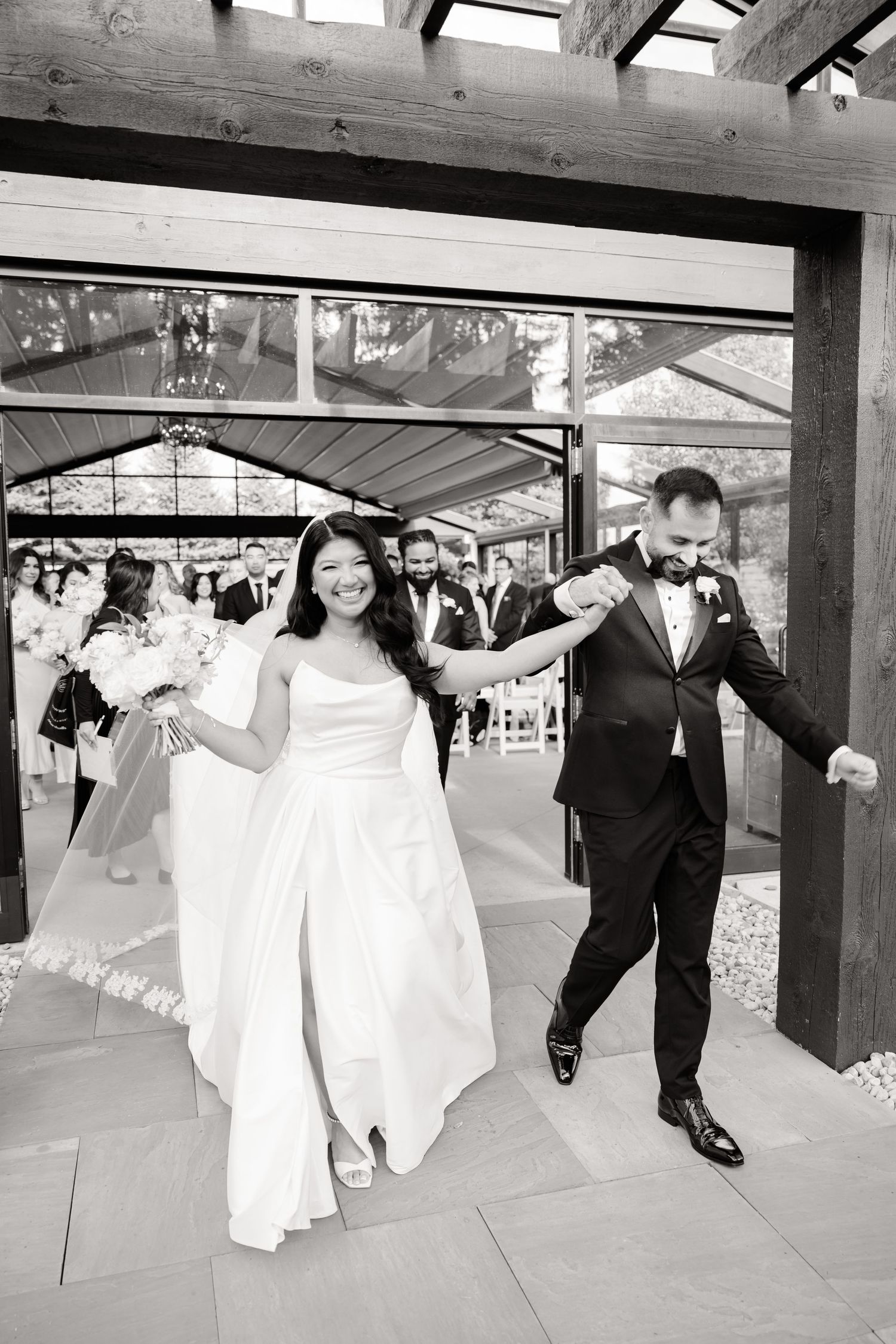 A celebratory wedding exit through wooden beams in black and white photography.