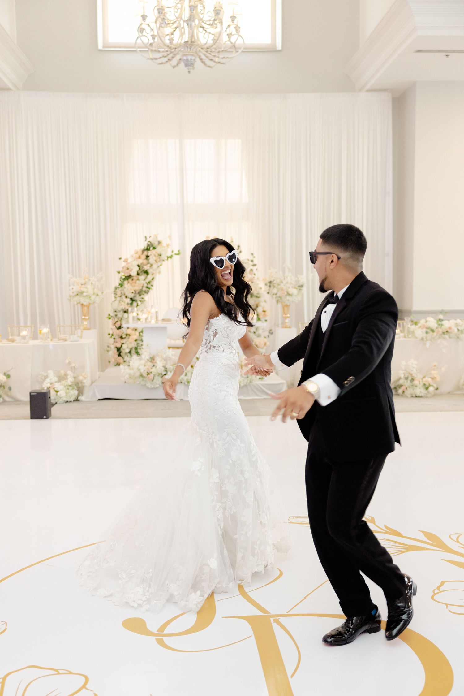 A fun dance moment at a wedding with sunglasses and elegant decor on a white and gold floor.
