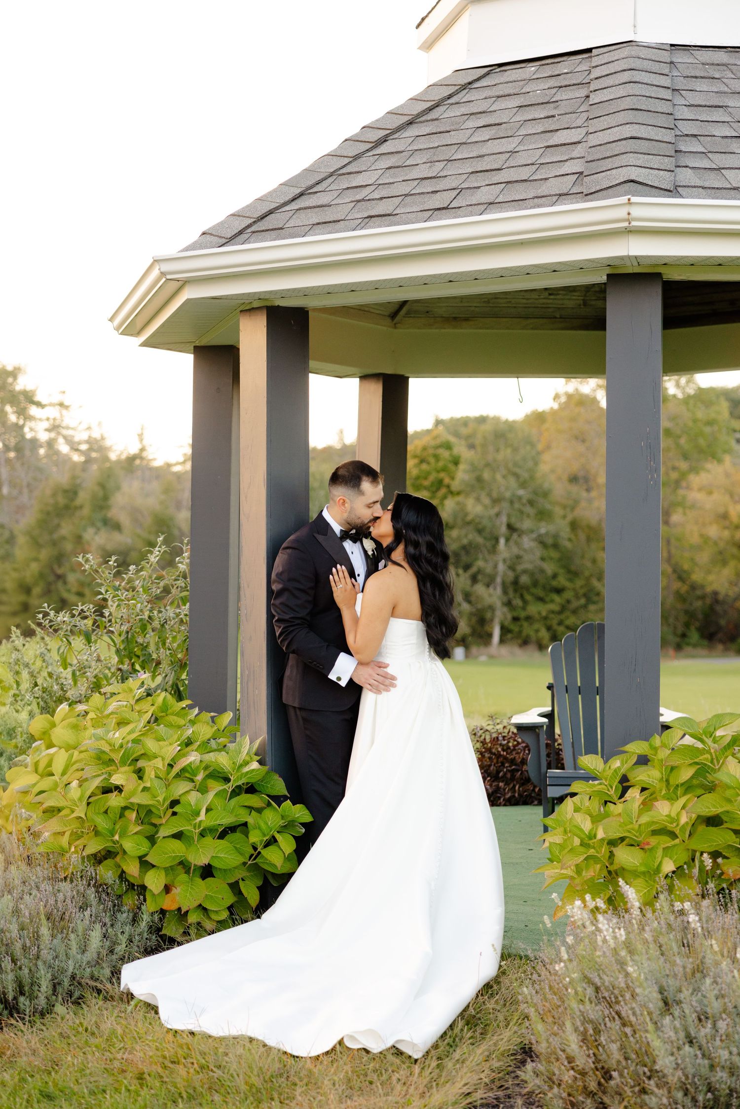 Wedding couple embraces in a scenic garden gazebo with beautiful landscaping.