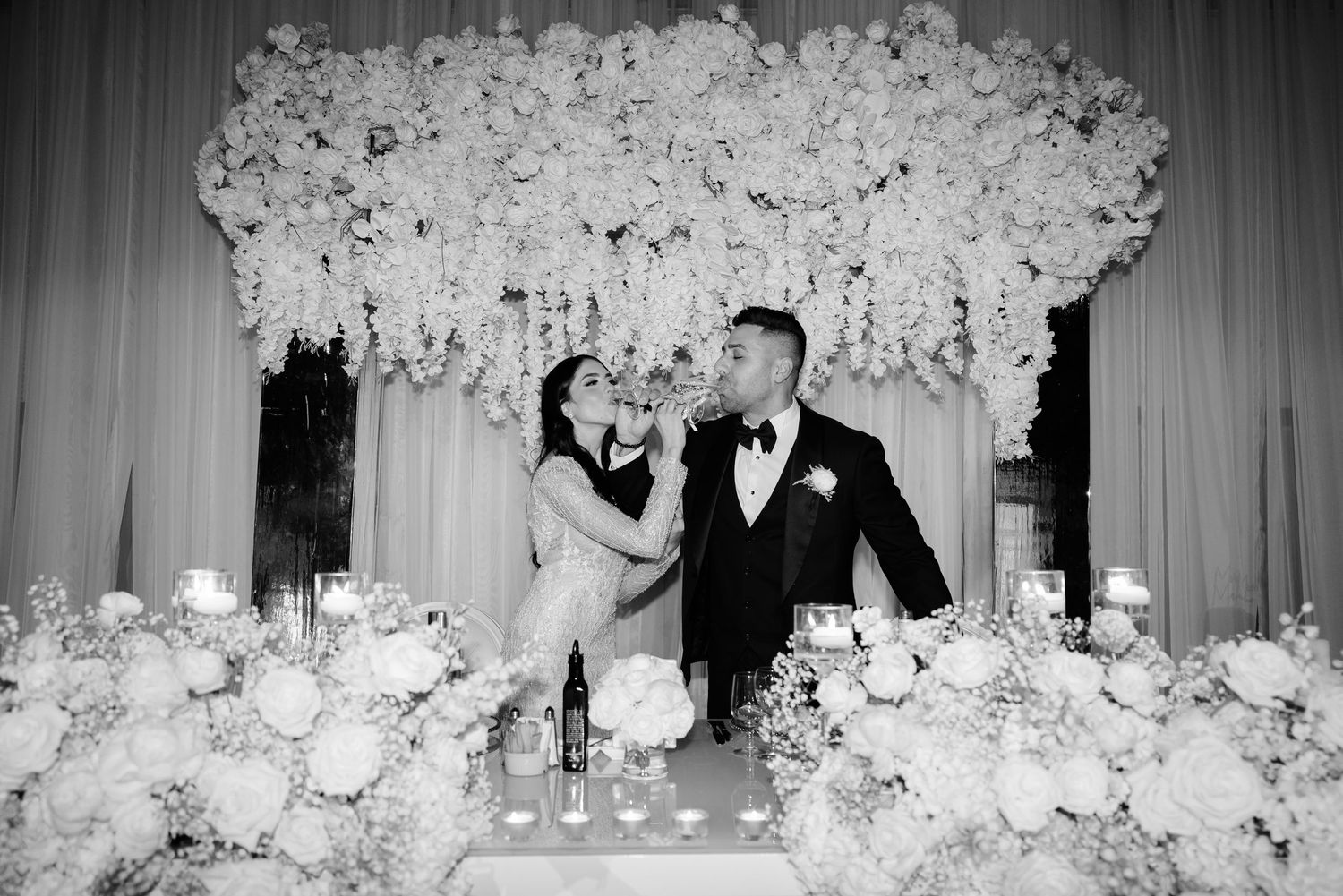 Newlyweds toast at their elegant reception beneath a cascade of white flowers.