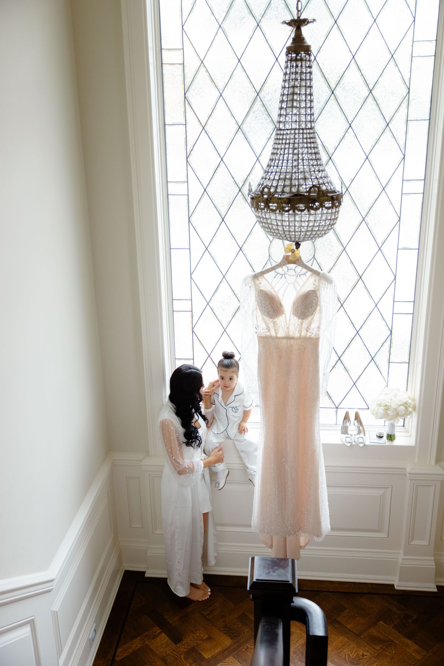 Wedding dress hanging from crystal chandelier as two figures interact below.