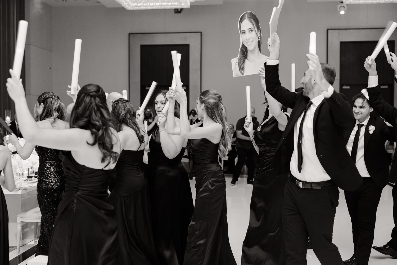 Large group of people in a black and white photo raising their hands in unison during what appears to be a meeting.