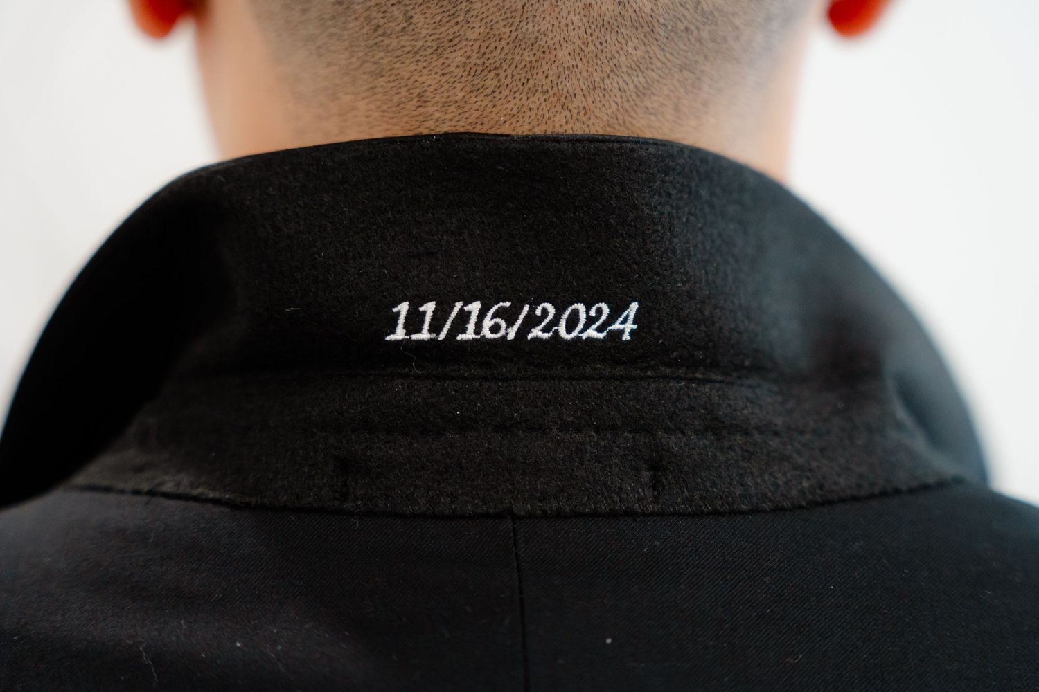 Close-up view of a black shirt collar with date 11/16/2024 embroidered in white thread.