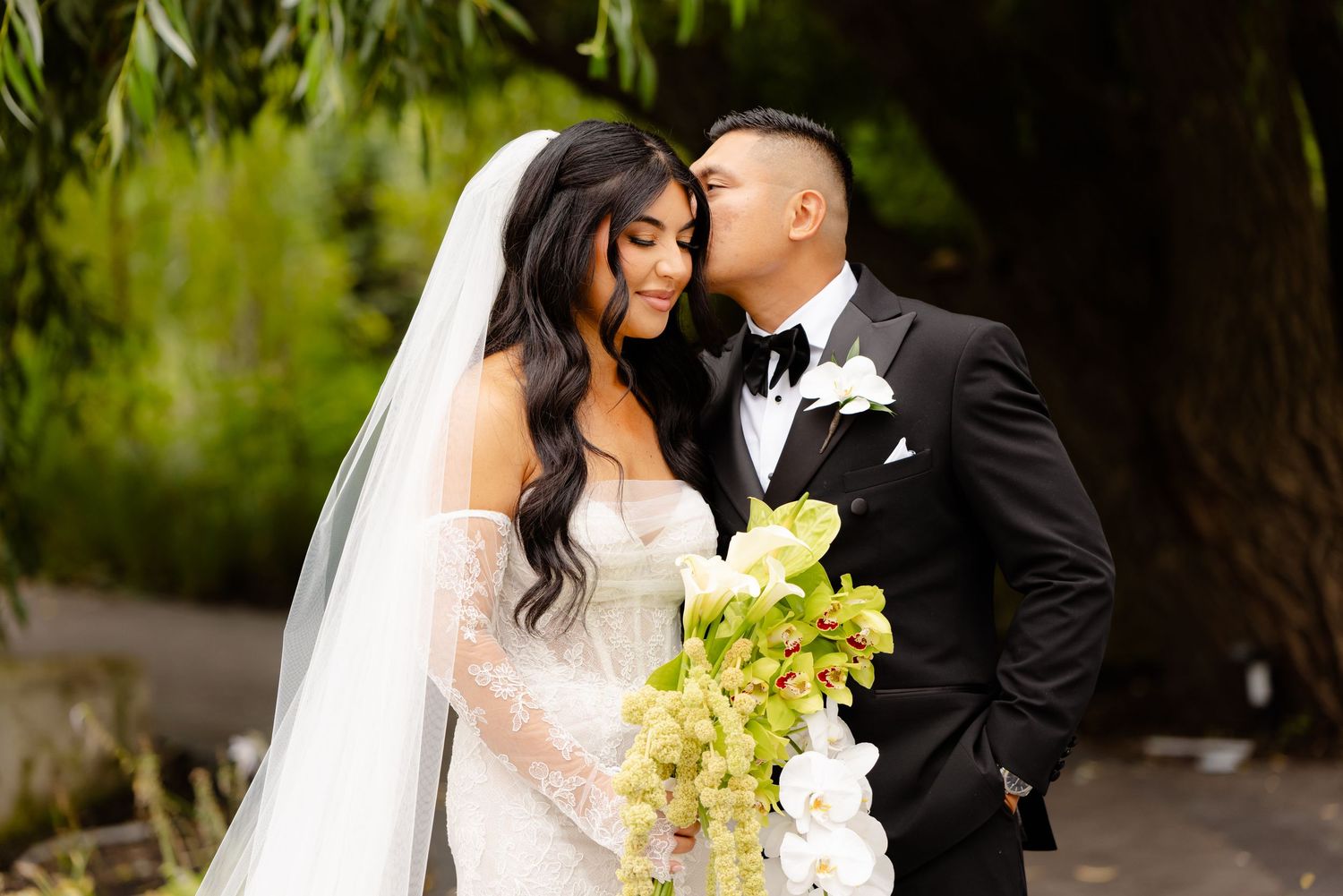 A couple shares romantic moments during their wedding day amongst lush greenery while wearing traditional formal attire.