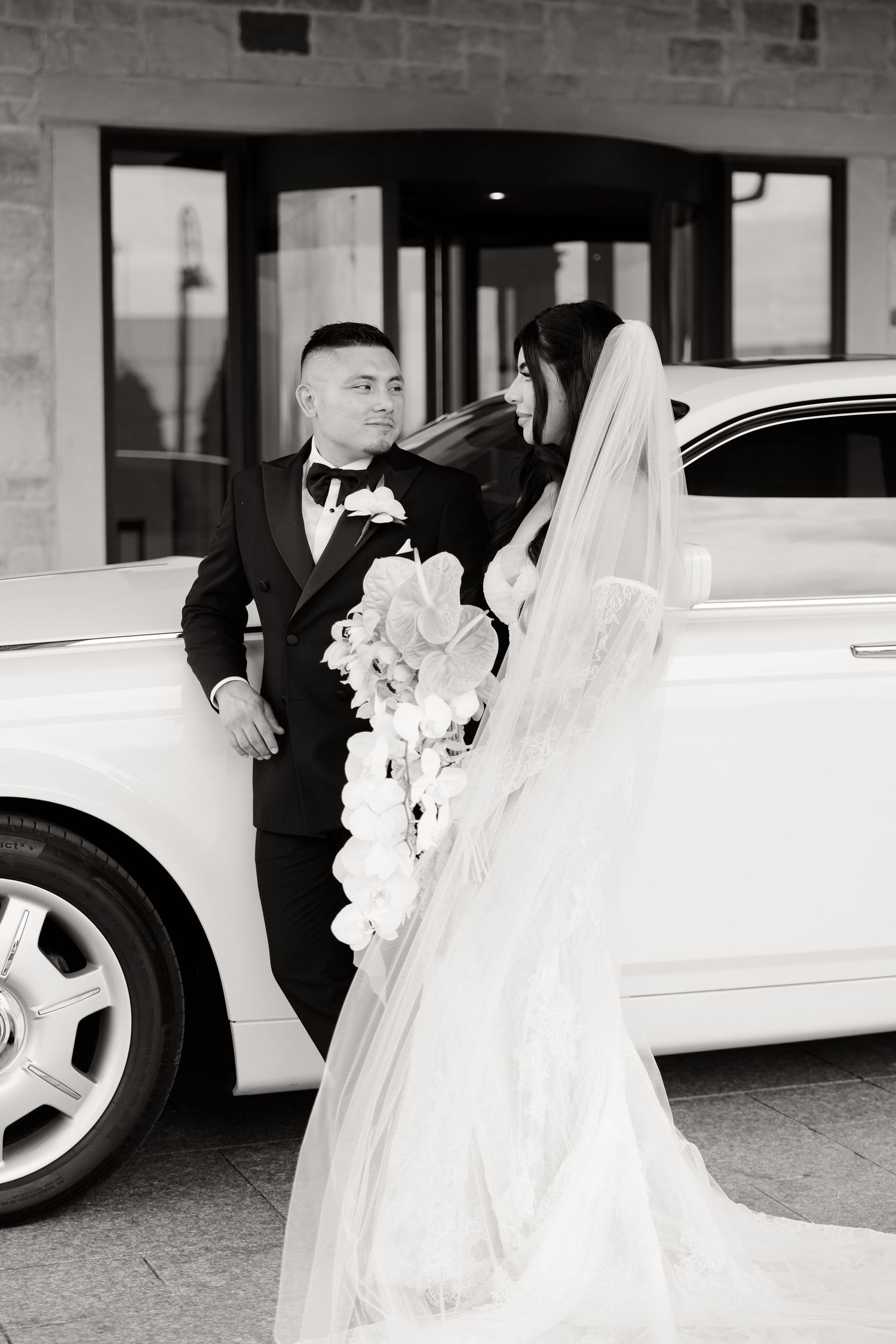Elegant white Rolls Royce wedding car parked under covered entrance with couple in formal attire.