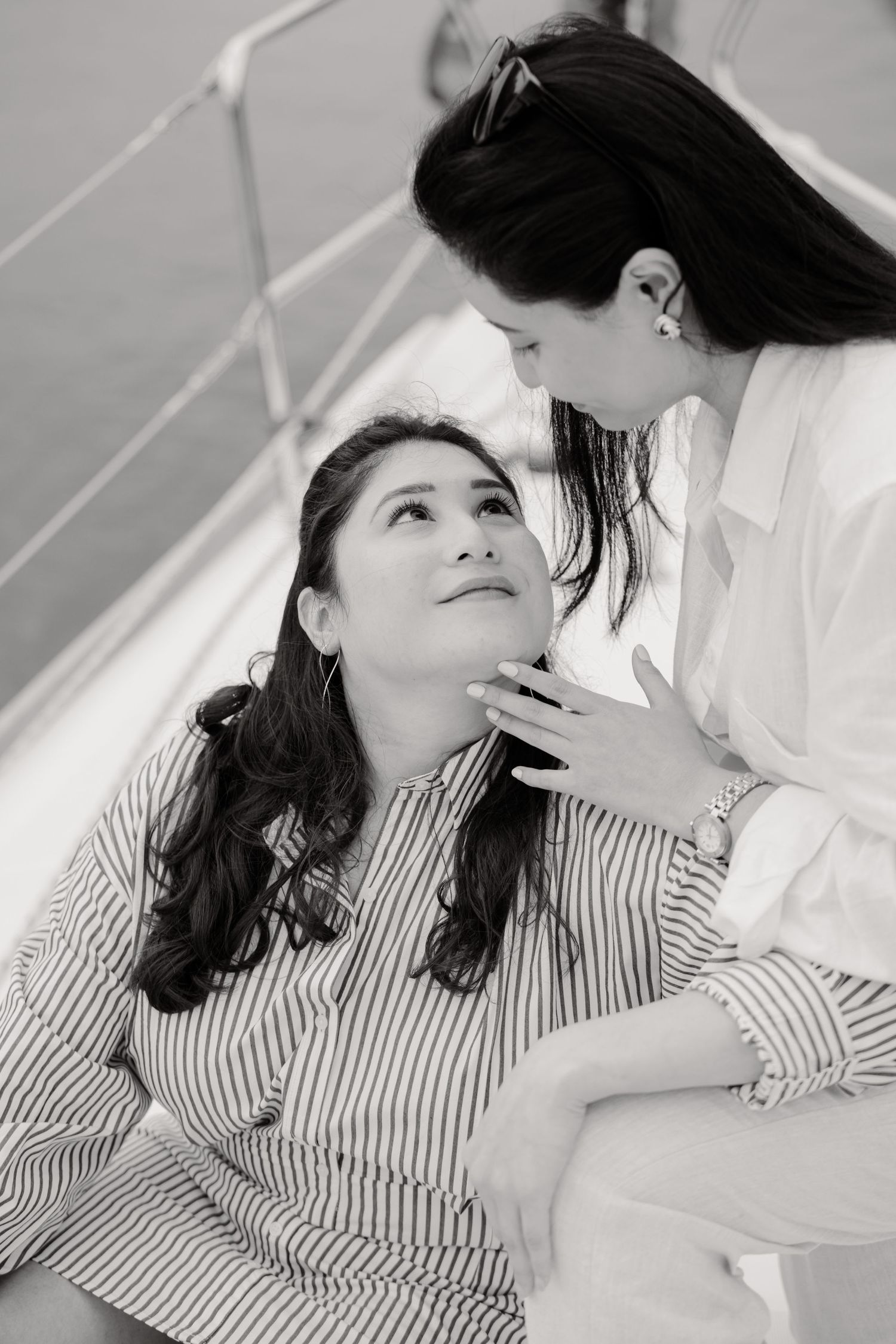 A black and white image of two women in intimate conversation, one sitting and one standing in white attire.