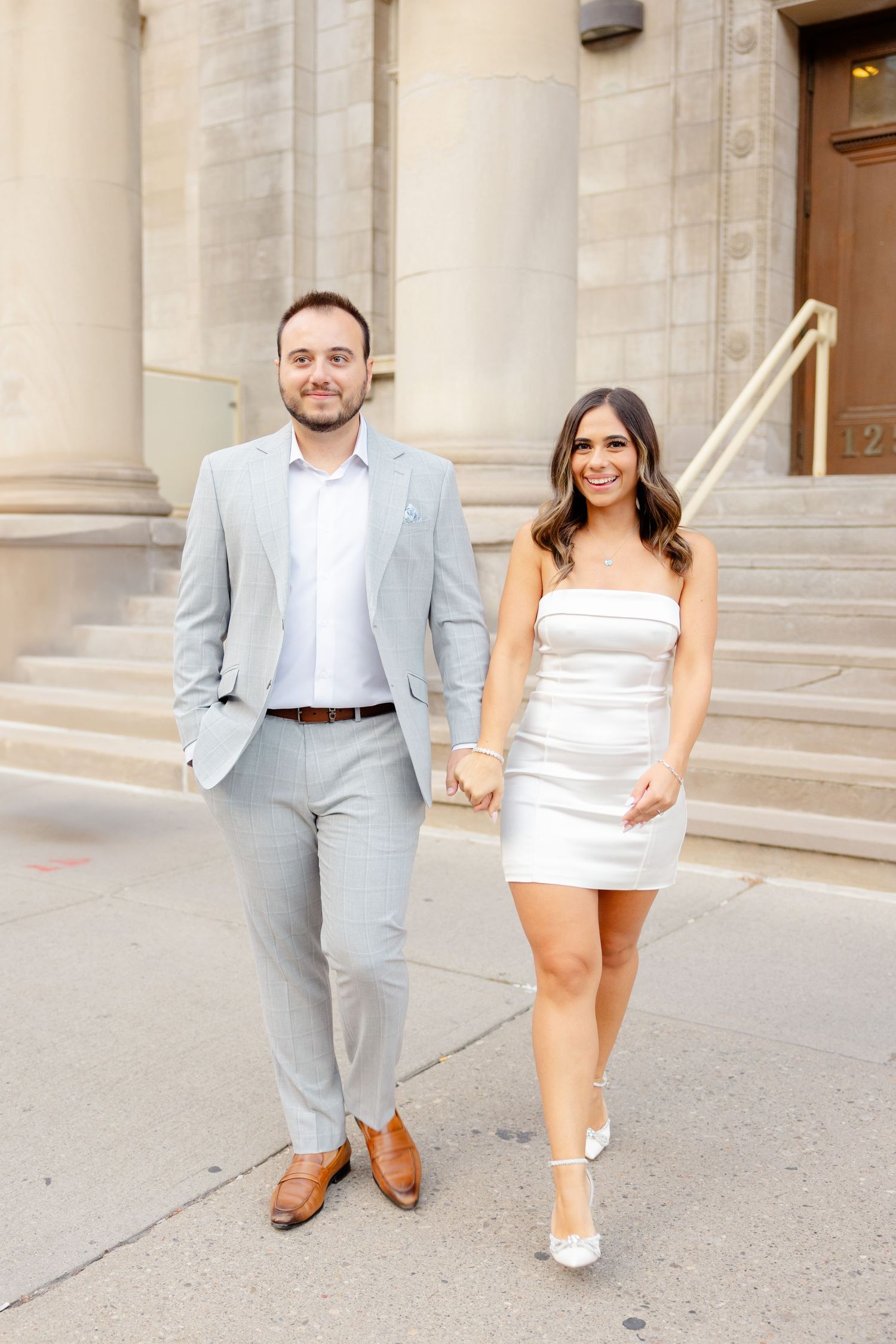 A couple in light summer formal wear poses together on stone steps.