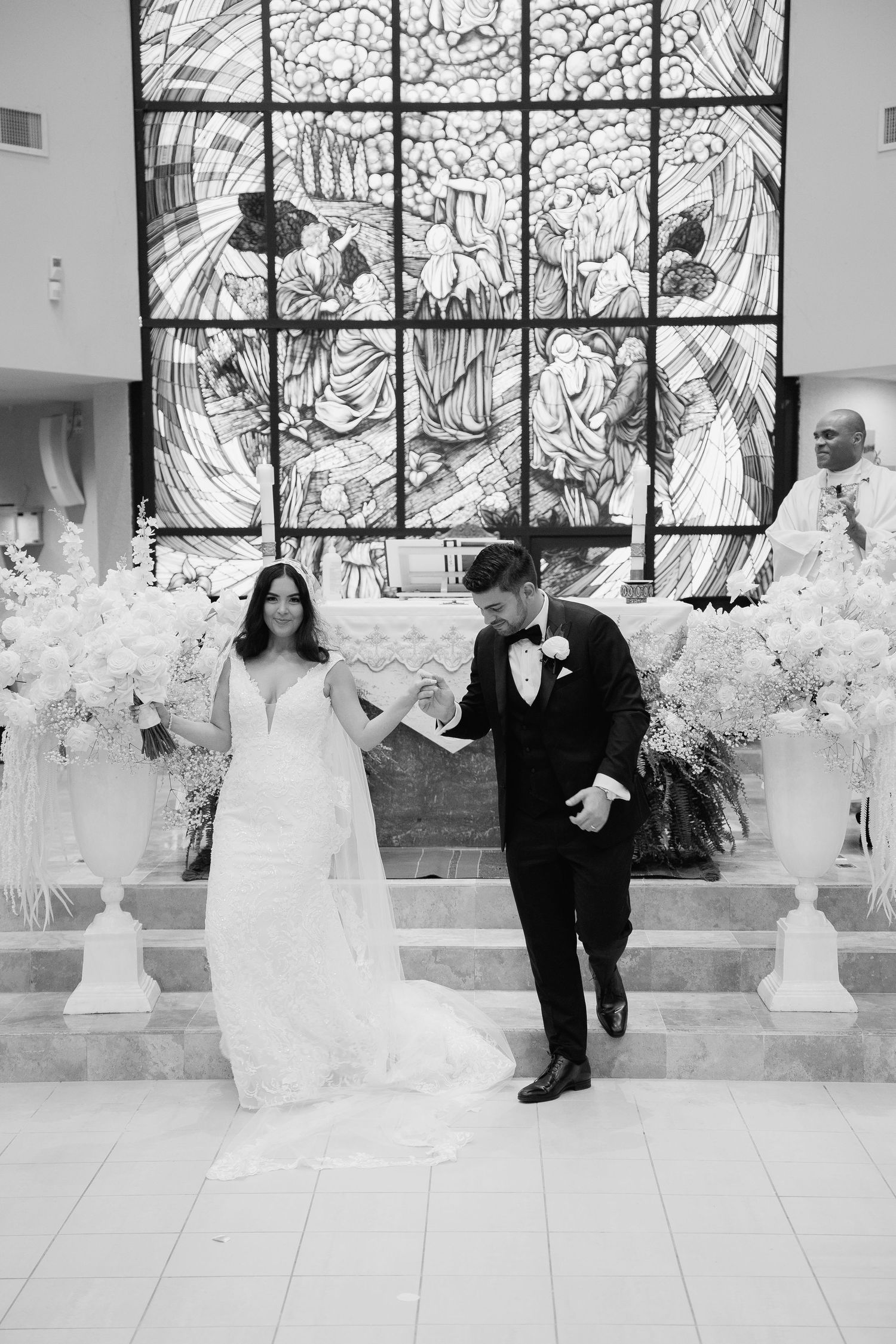 Black and white photo of newlyweds celebrating in church with stained glass backdrop.