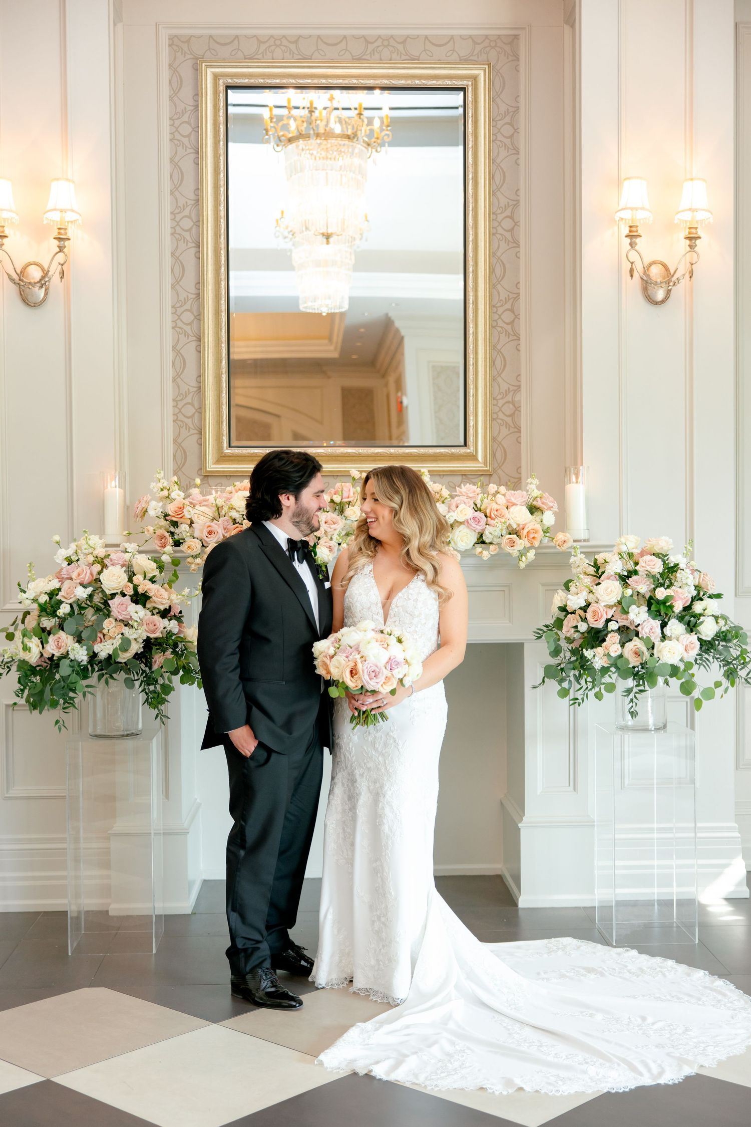 Romantic wedding portrait scene with gold-framed mirror and floral arrangements.