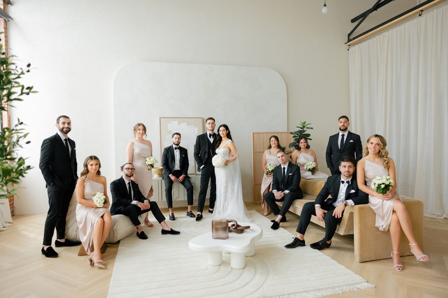 Wedding party posed together in elegant white room with modern furnishings.