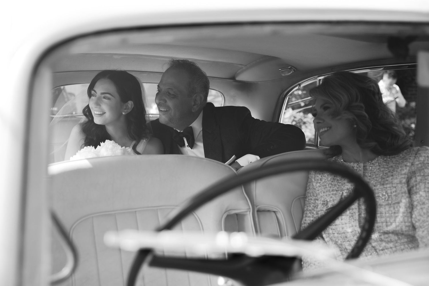 A vintage-style black and white photograph showing passengers smiling together inside a classic car.