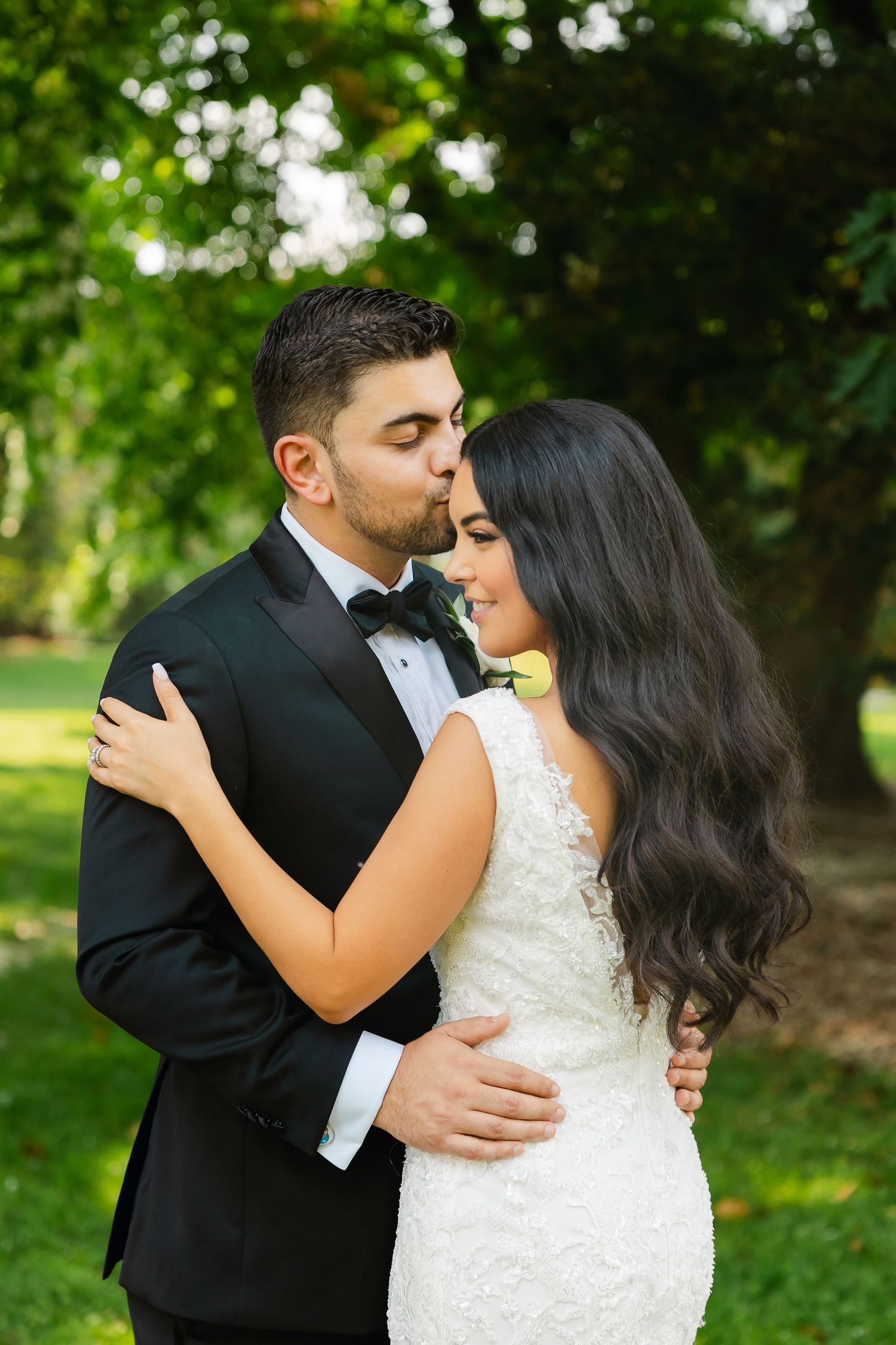 Romantic garden wedding photo of couple sharing a tender moment among green foliage.