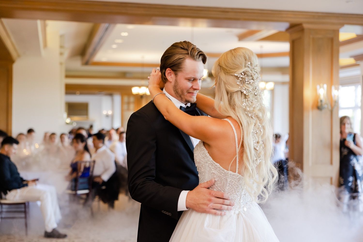 Intimate dance moment captured in a sunlit ballroom with elegant chandeliers and wooden beams.