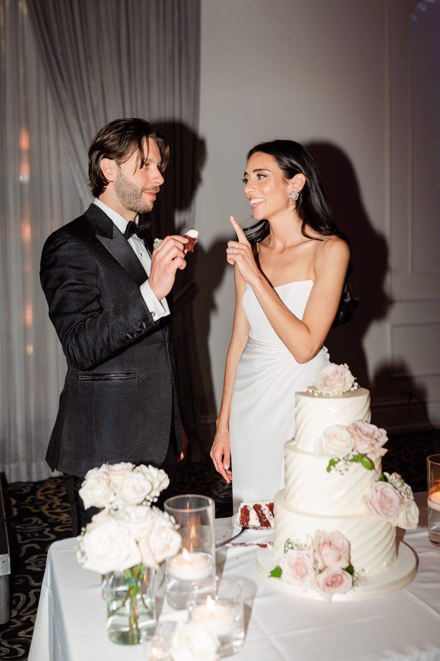 Newlywed couple share a playful moment while feeding each other wedding cake at their elegant reception.