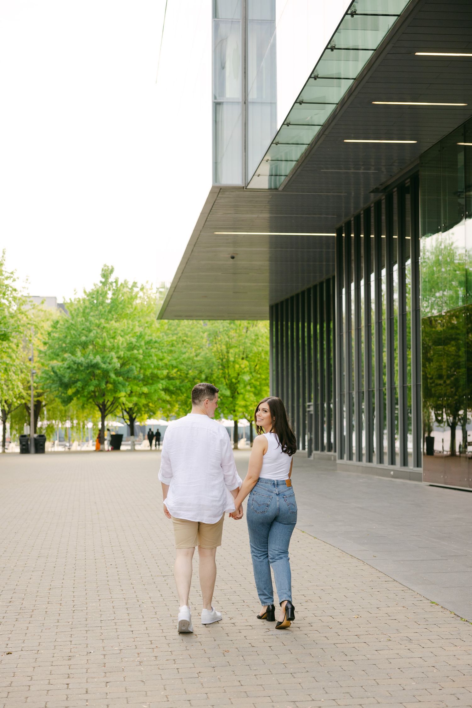 A couple in casual attire walking hand in hand near a contemporary building exterior.