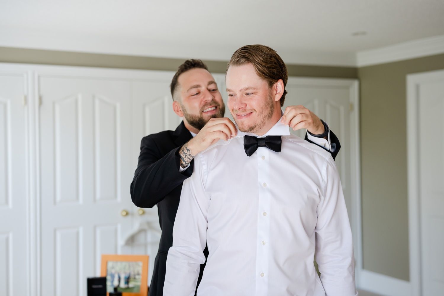 Two people in formal wear helping with bow tie and clothing adjustments.