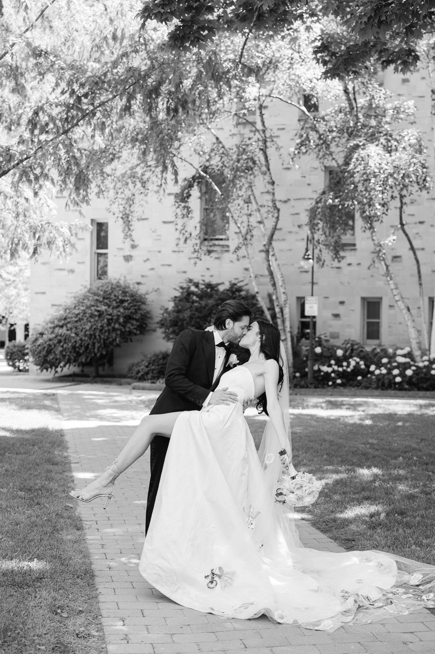 Black and white romantic dip pose of newlyweds on brick pathway with historic building backdrop.
