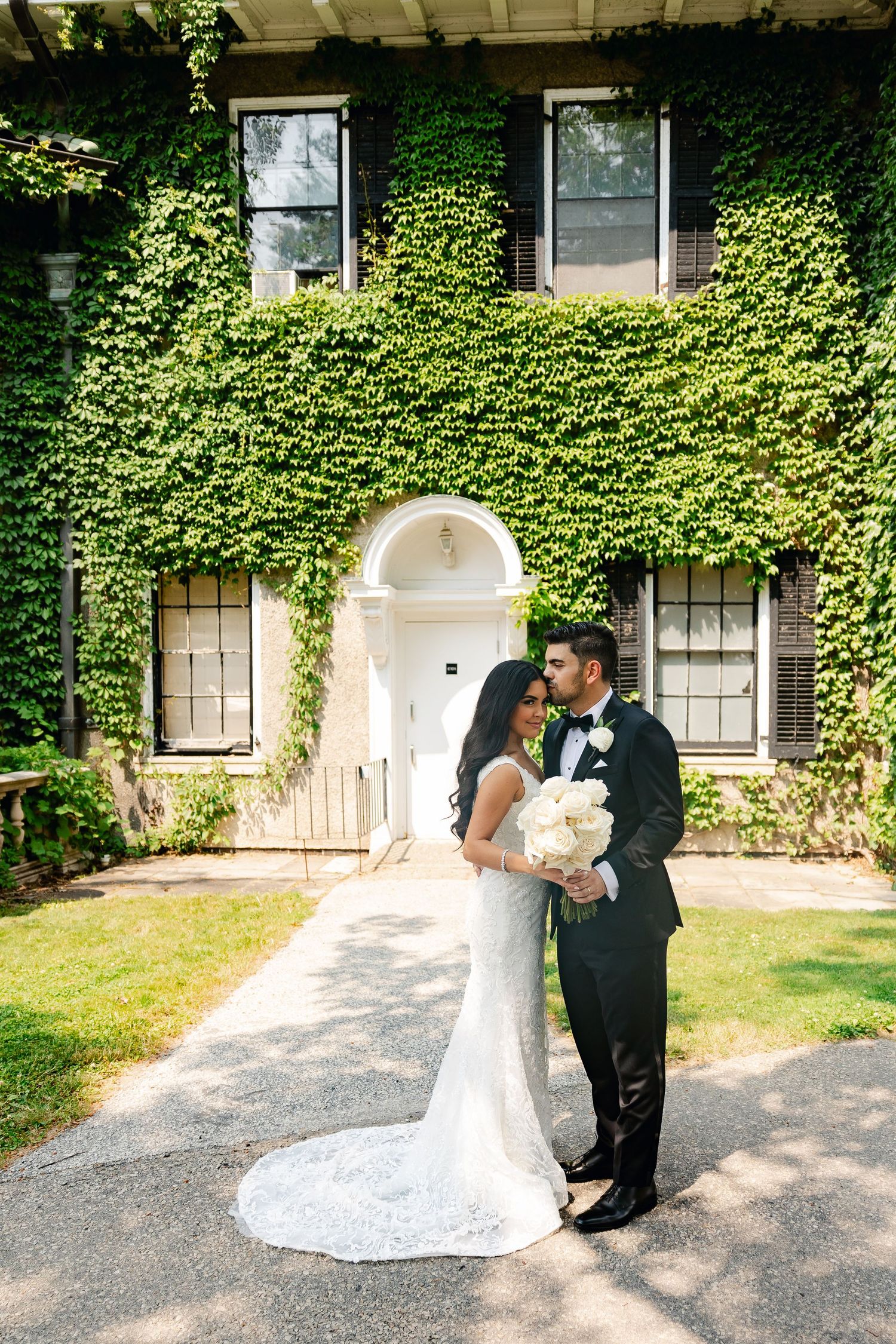 Wedding couple poses in front of ivy-covered historic building with white arched doorway.