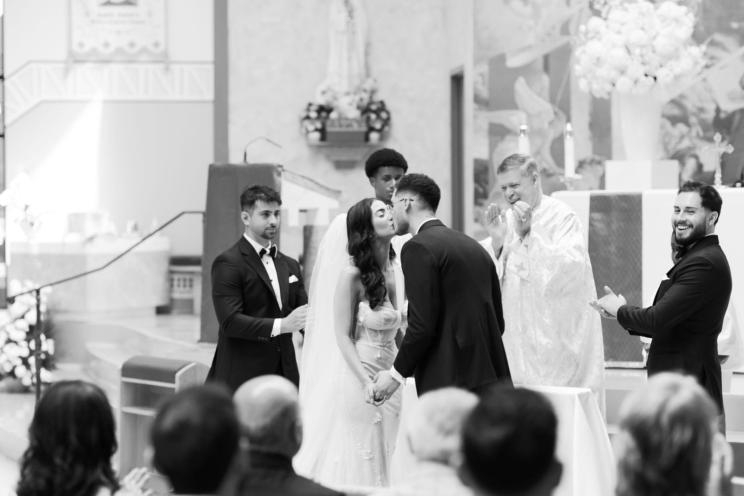 A candid black and white shot of a wedding ceremony in progress at a Catholic church.