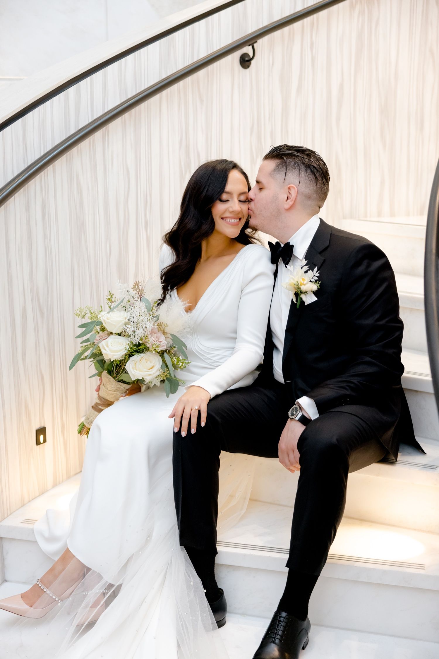 Intimate wedding moment captured on modern white staircase with curved railing details.