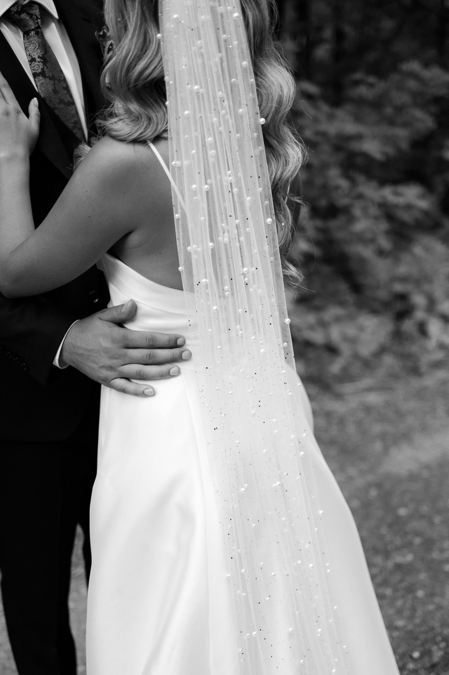 Close-up detail of sparkly wedding veil and classic white dress during intimate moment.