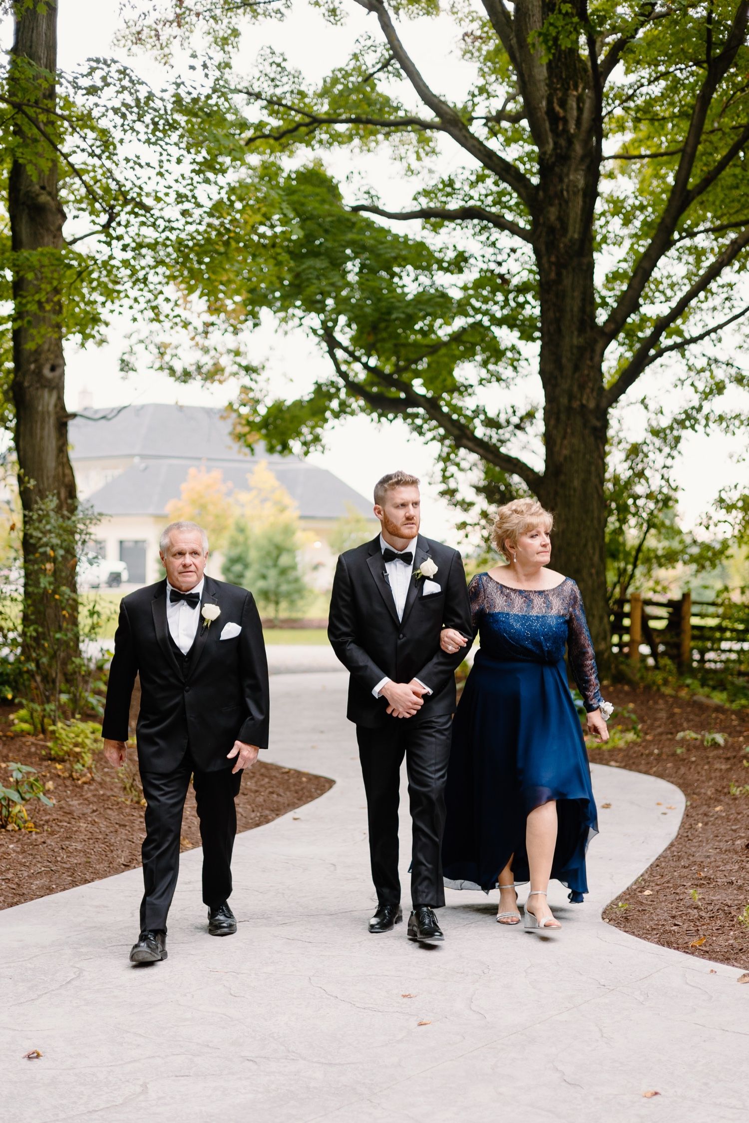 Wedding ceremony processional on a winding garden path surrounded by lush trees.