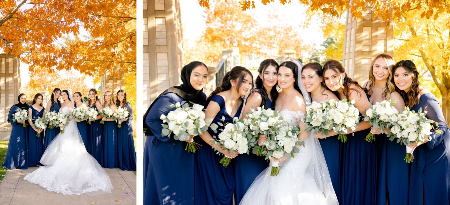 Wedding party members in navy blue attire pose together under bright autumn trees.