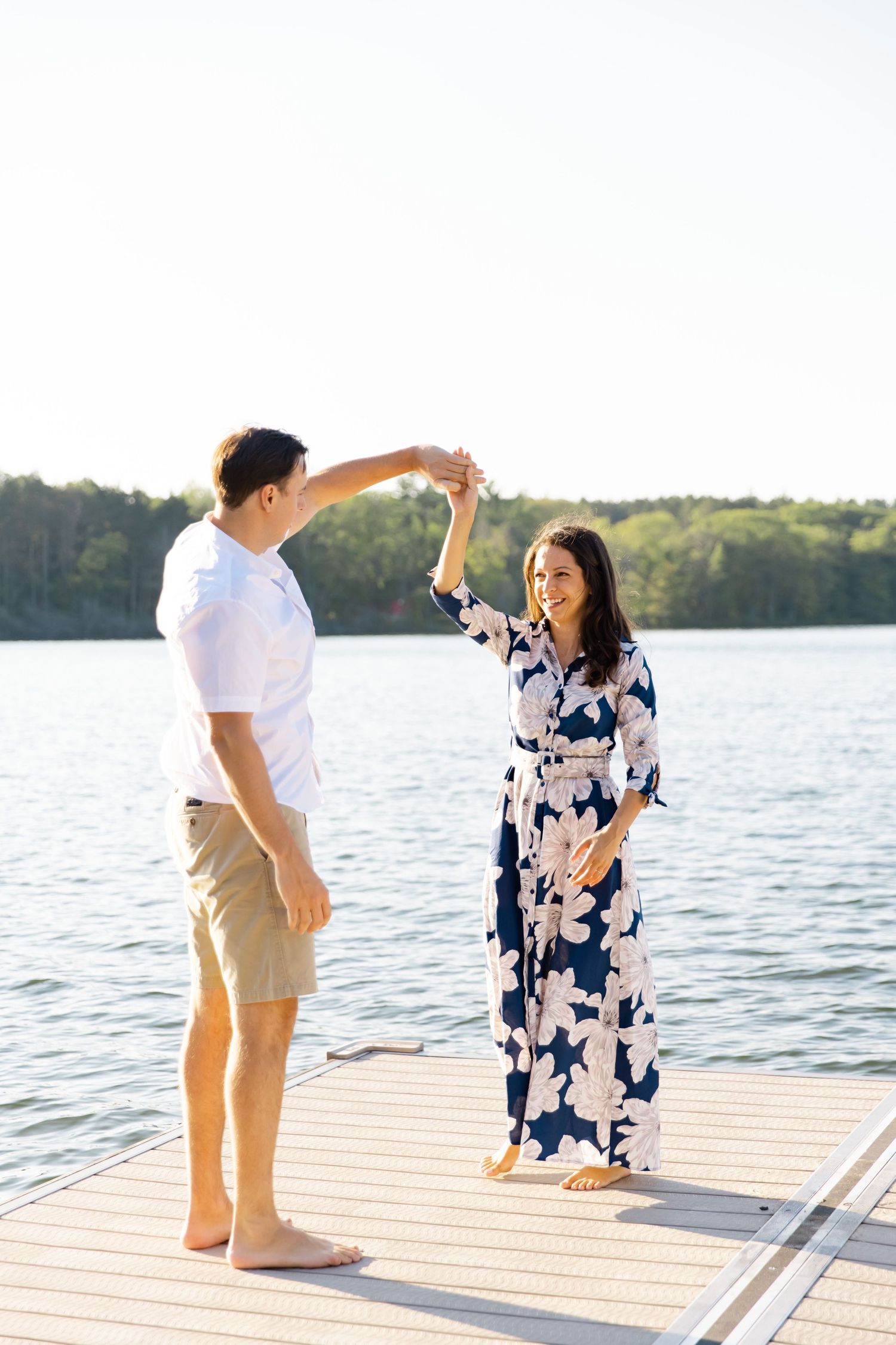 A couple dances together on a wooden dock with a scenic lake view in the background.