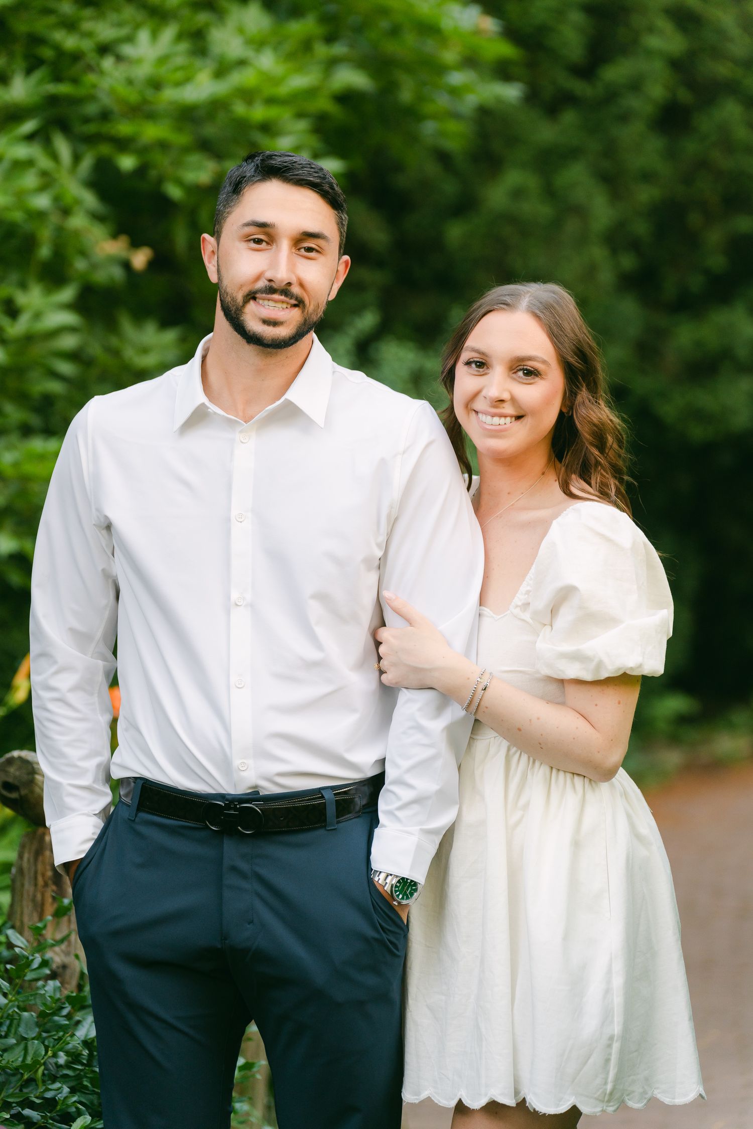 Couple in coordinated white outfits standing together on garden pathway.