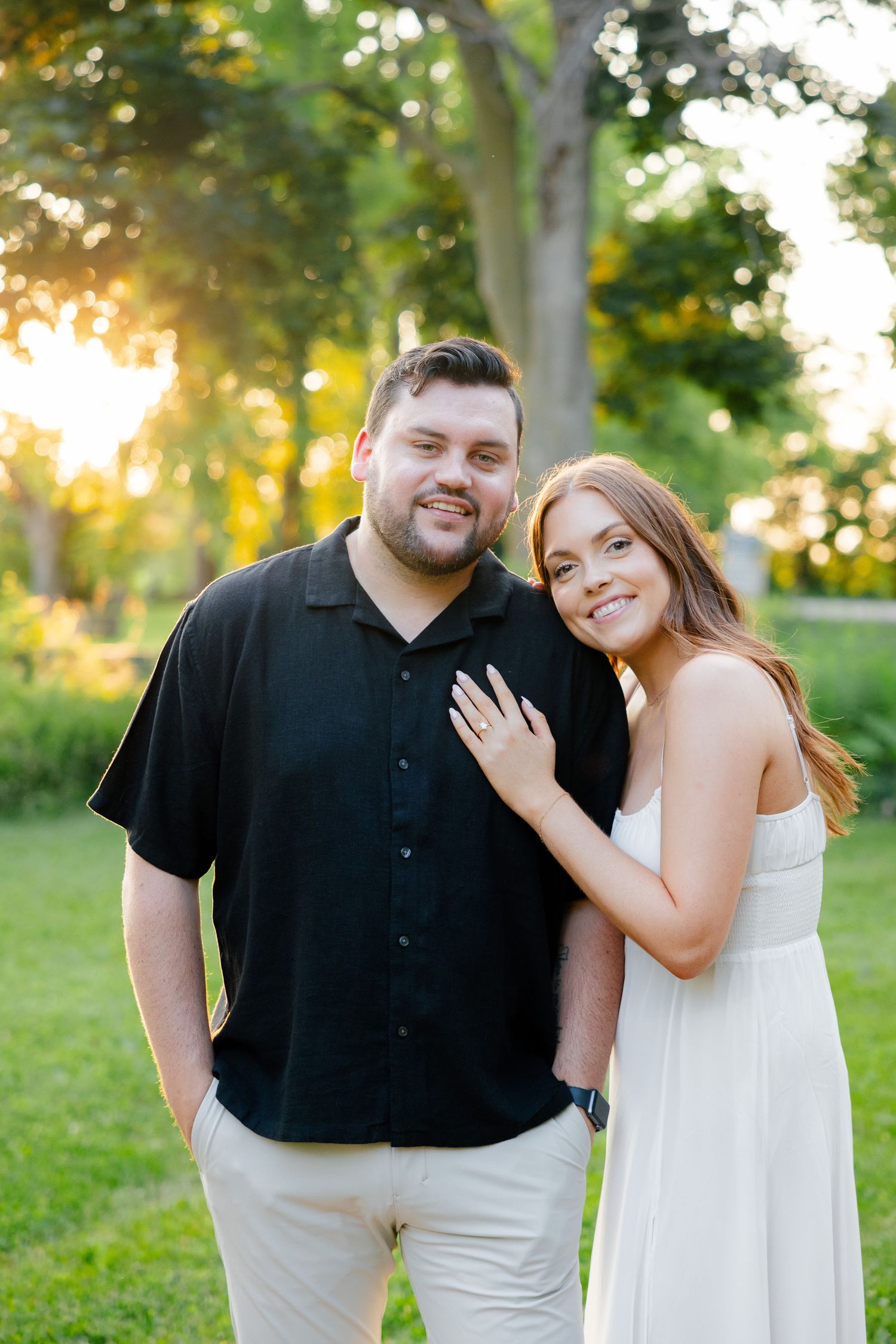 Happy couple poses together in summer park setting during golden hour.