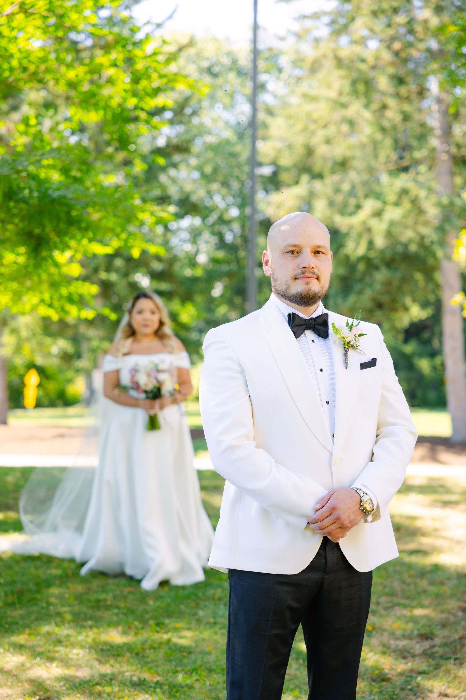 Elegant couple poses separately for wedding portrait in sunlit garden setting.