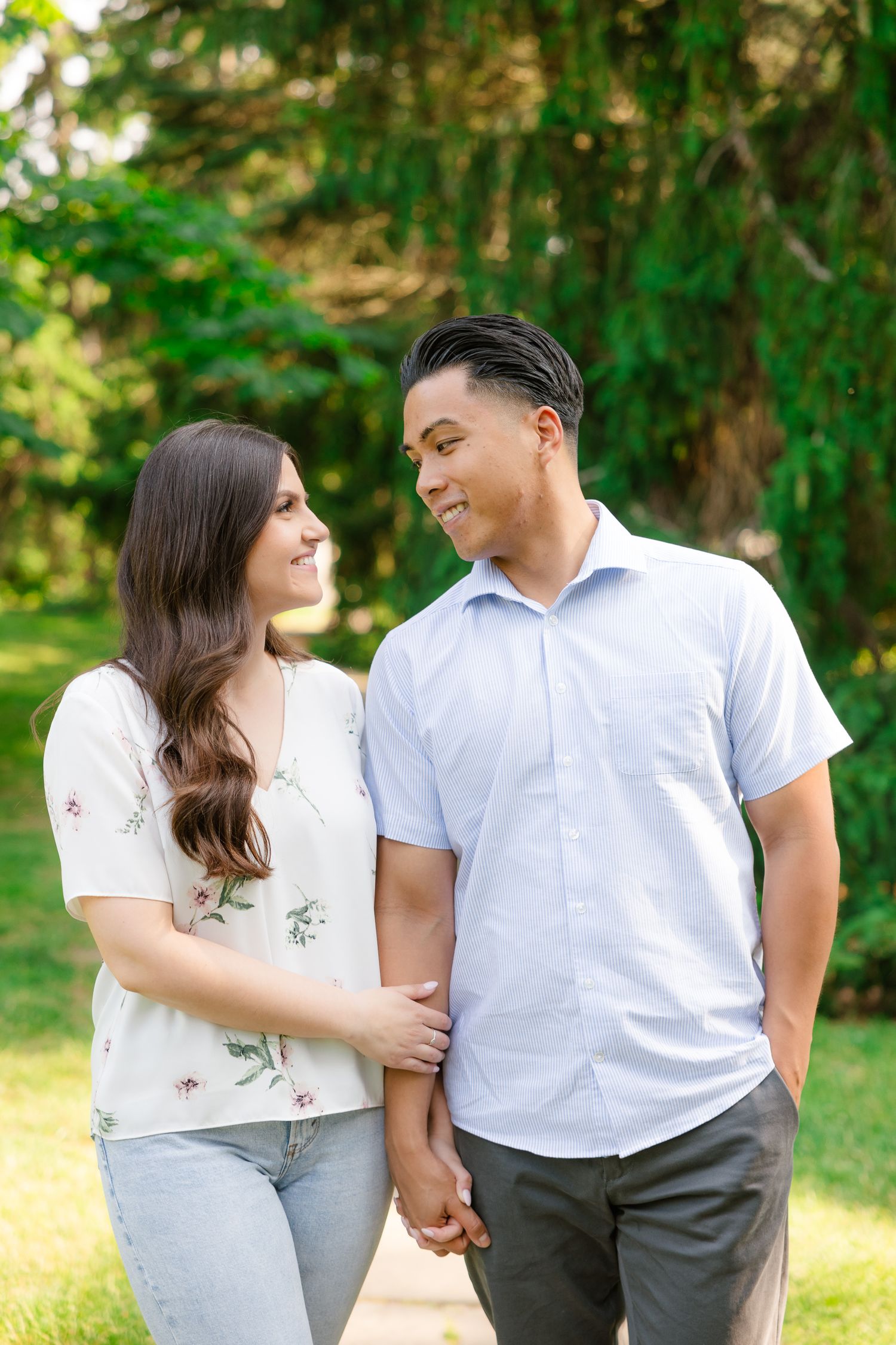A couple in casual attire holding hands while walking in a sunlit garden.
