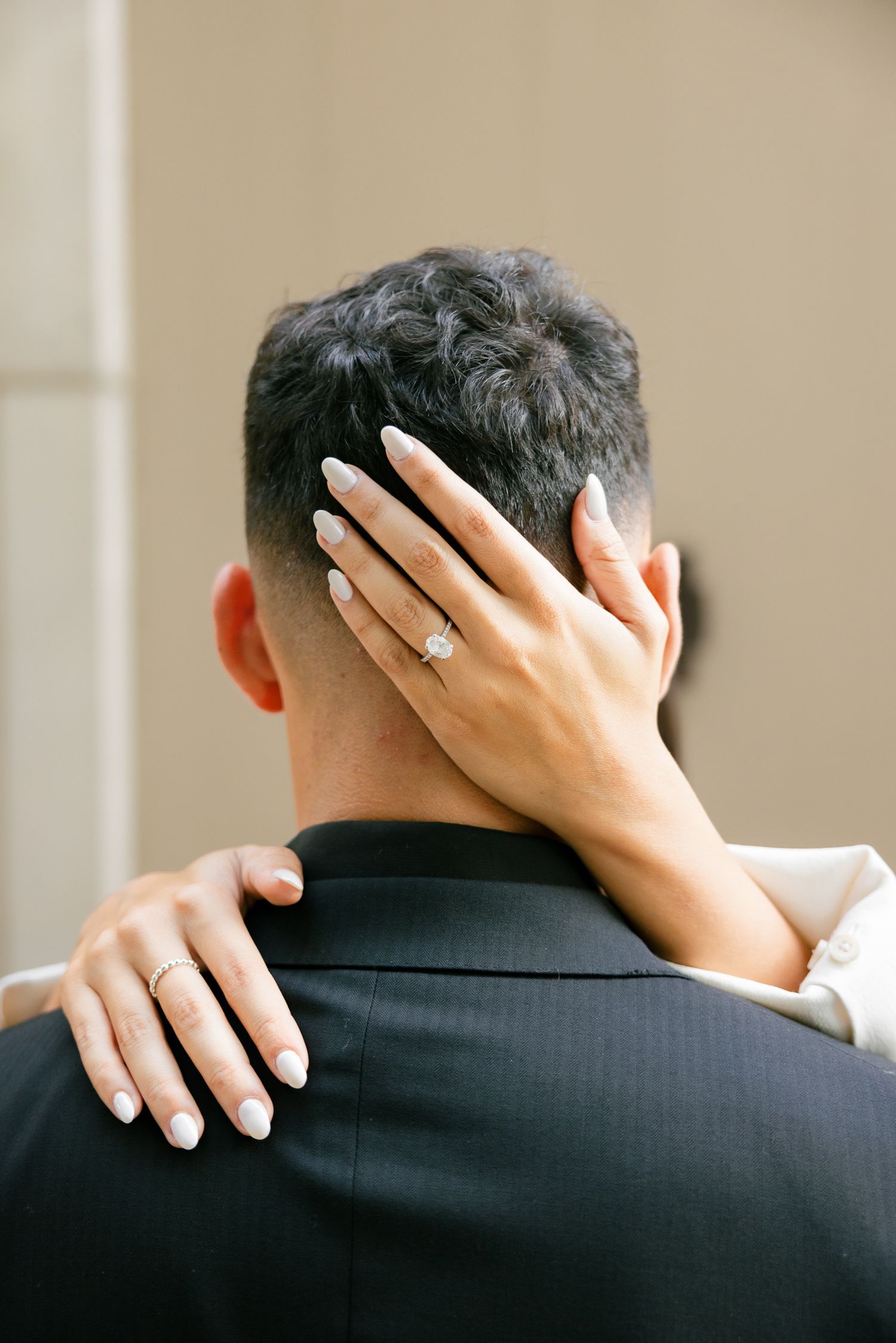 Close-up of hands with engagement ring embracing from behind.