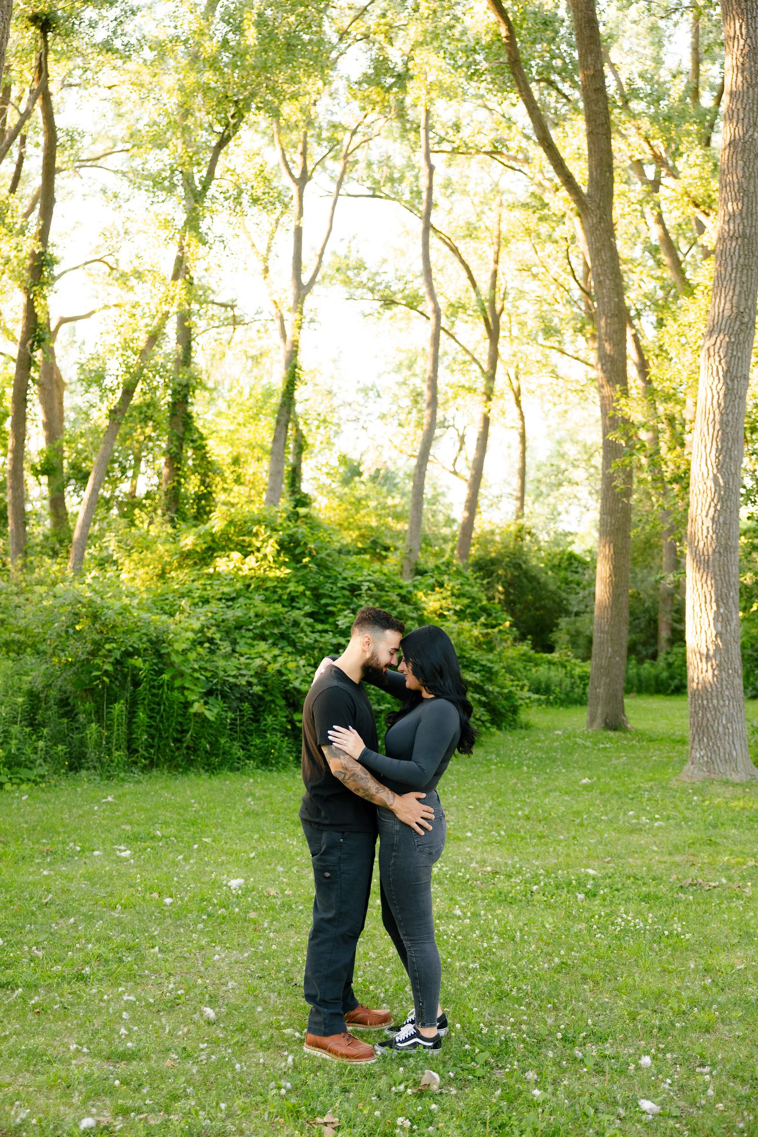 A couple embraces in an intimate moment surrounded by sunlit trees in a park setting.