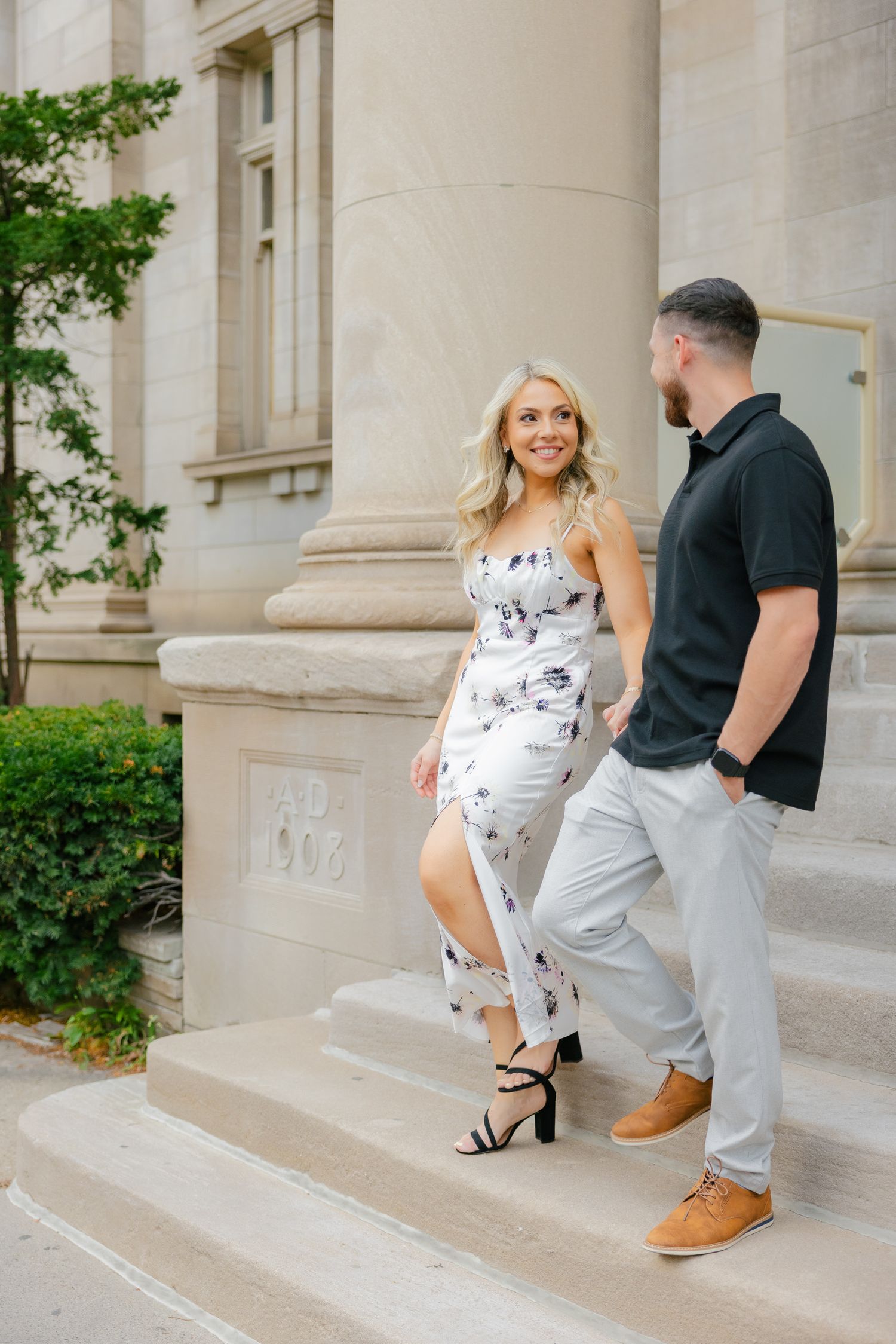 Two people ascending stone steps by classical columns, dressed in contrasting casual and dressy summer outfits.