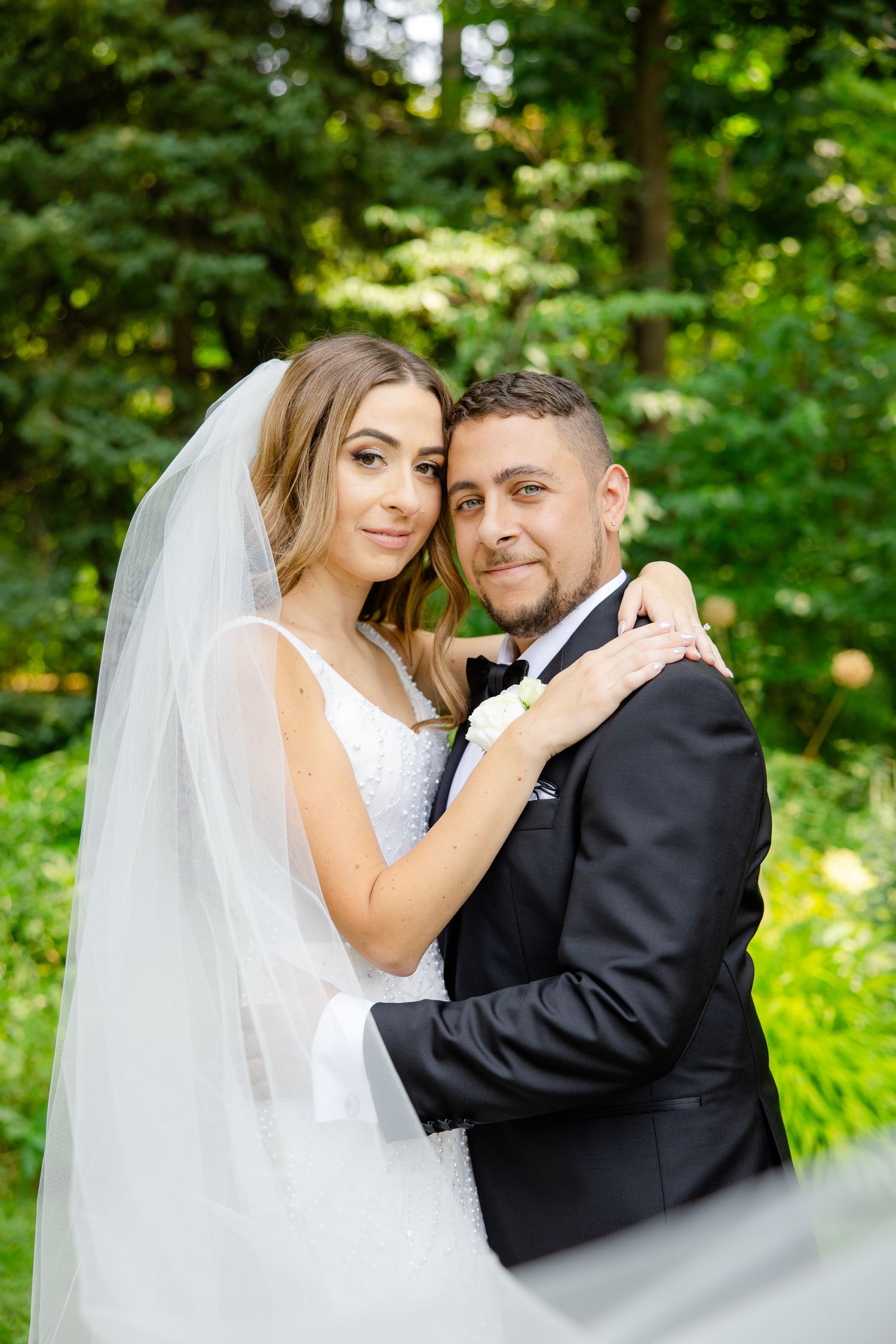 A romantic wedding portrait of newlyweds embracing in a lush green garden setting.