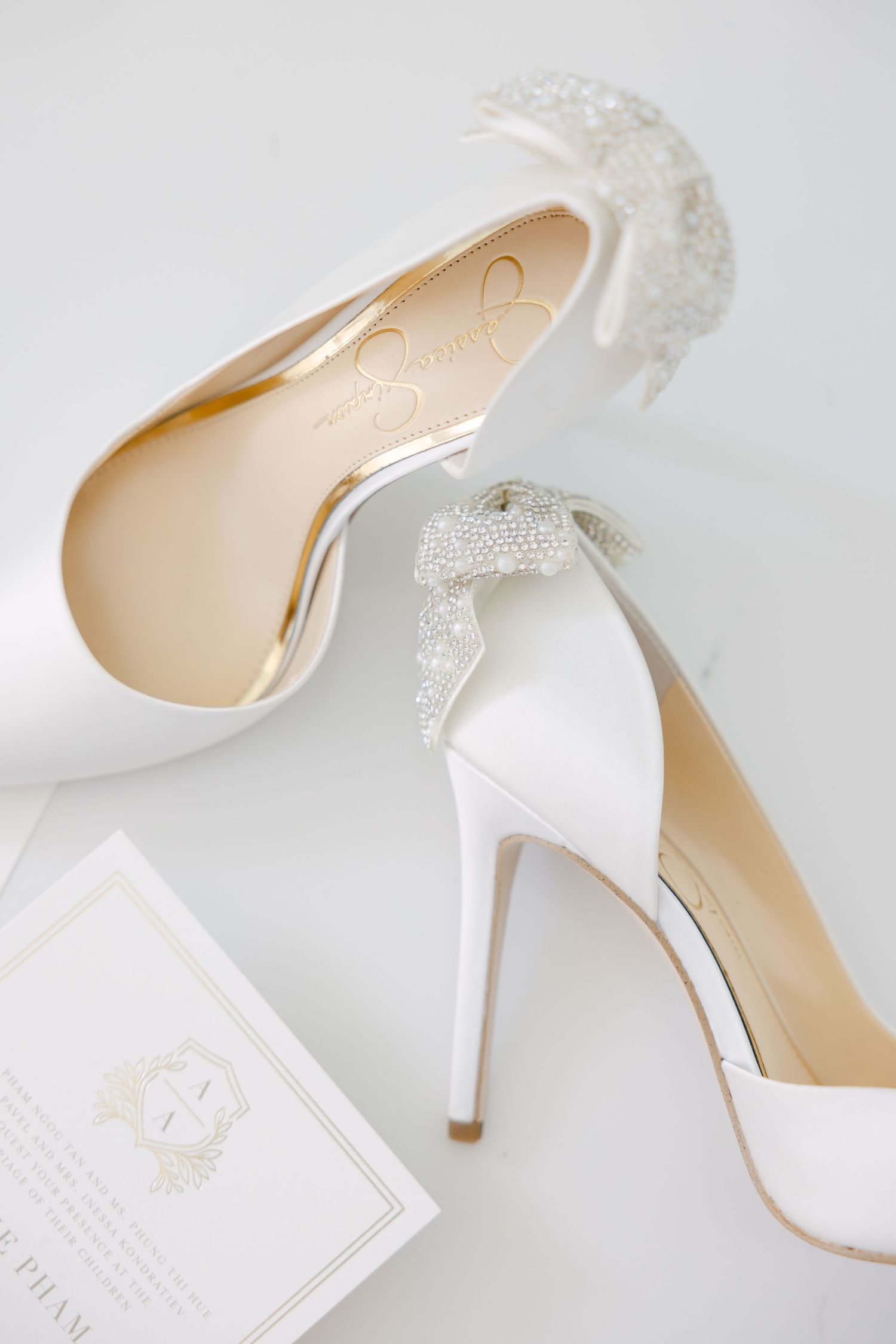 White bridal heels with crystal embellishments next to elegant wedding invitation.