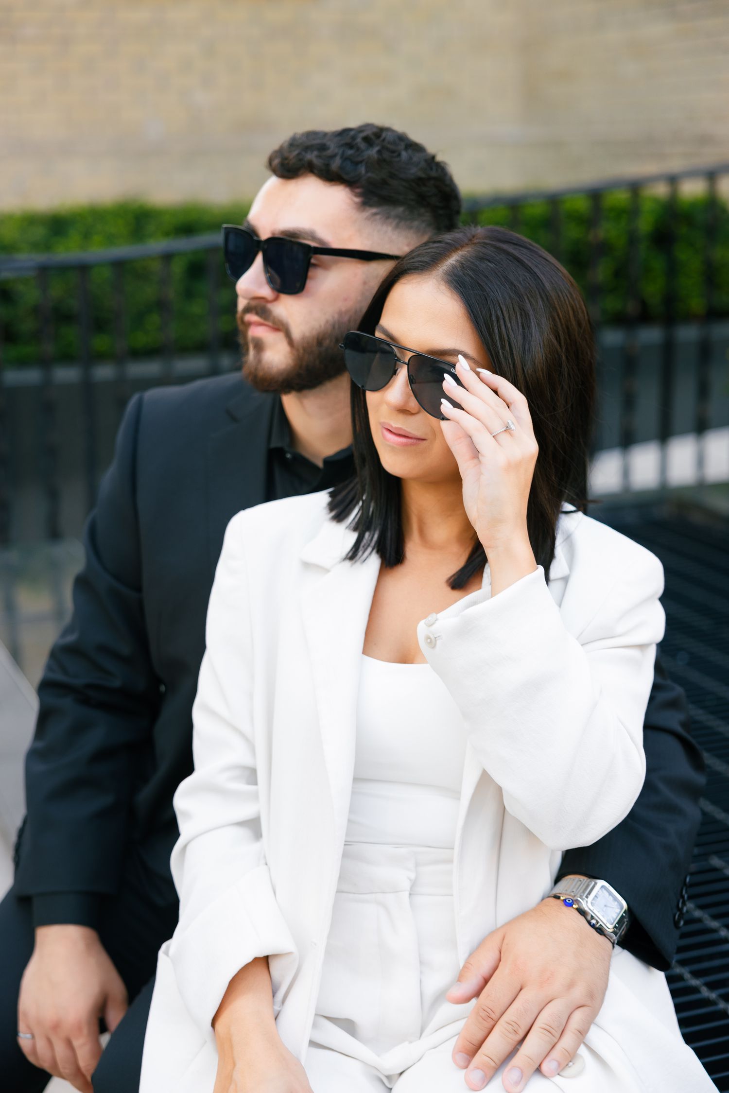 Sophisticated pair in contrasting suits pose with sunglasses at Chanel storefront.