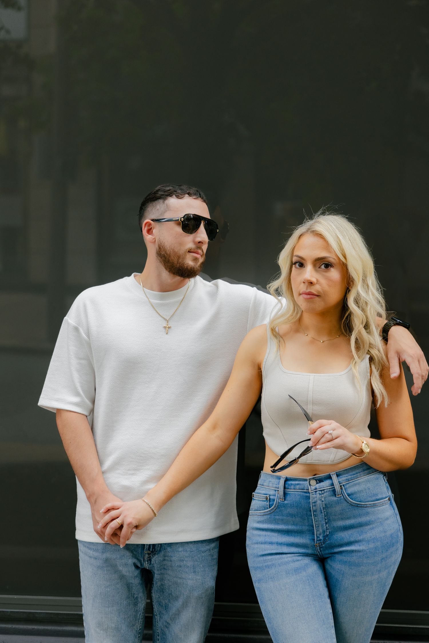 Fashion-forward couple in white and denim posing against dark urban backdrop.