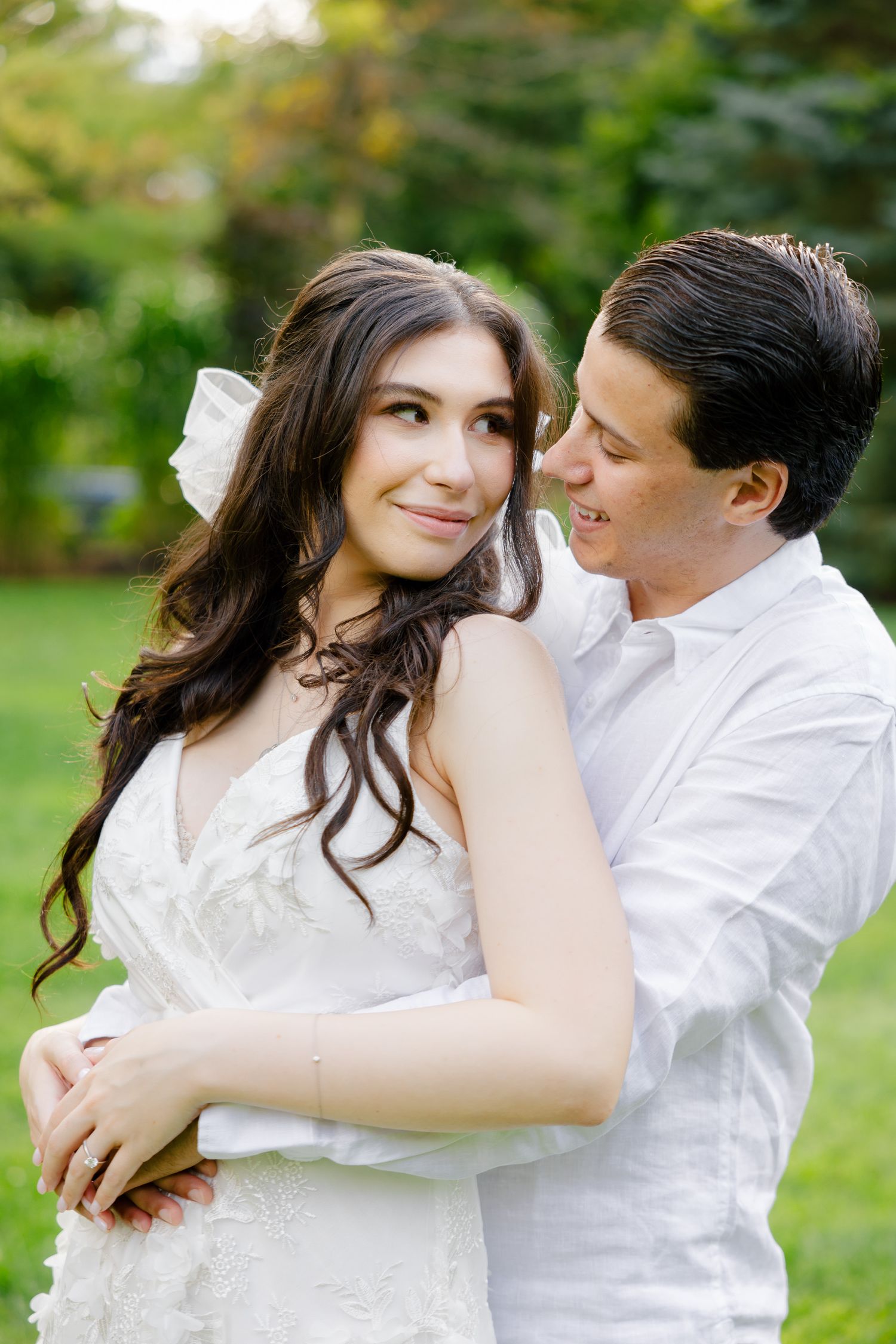 An intimate outdoor engagement photo of a couple in white clothing sharing a tender moment together.