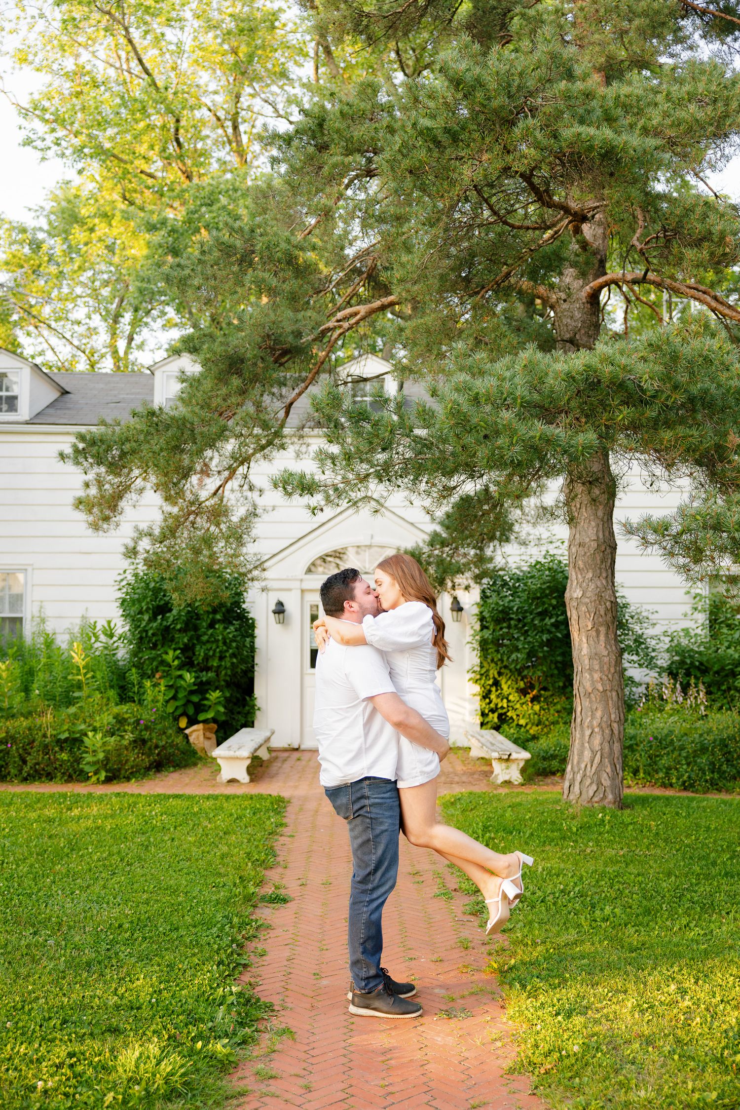 A joyful moment captured as a couple embraces on a brick pathway in front of a white building.