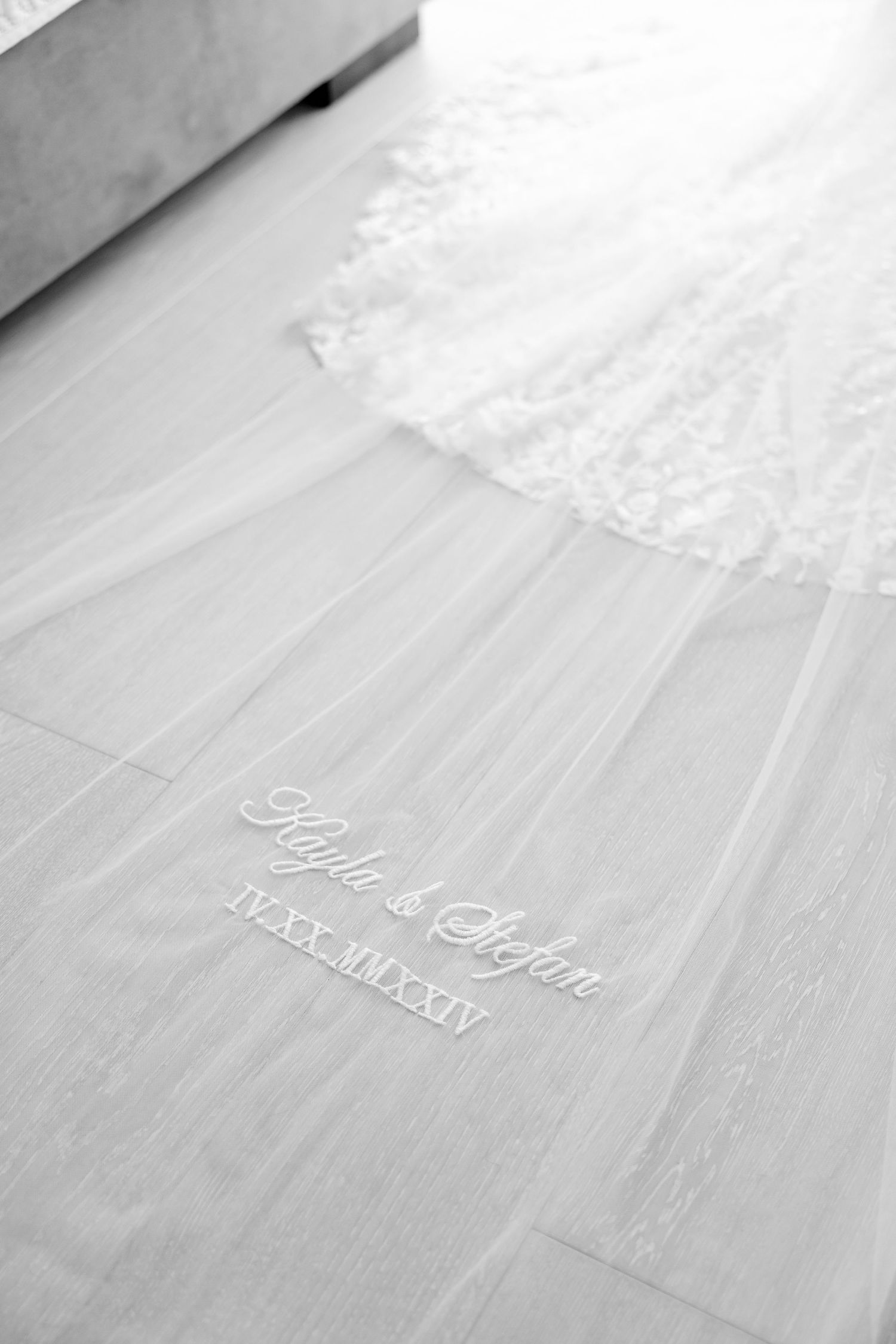 Close-up black and white photo of embroidered wedding veil details on wooden flooring.