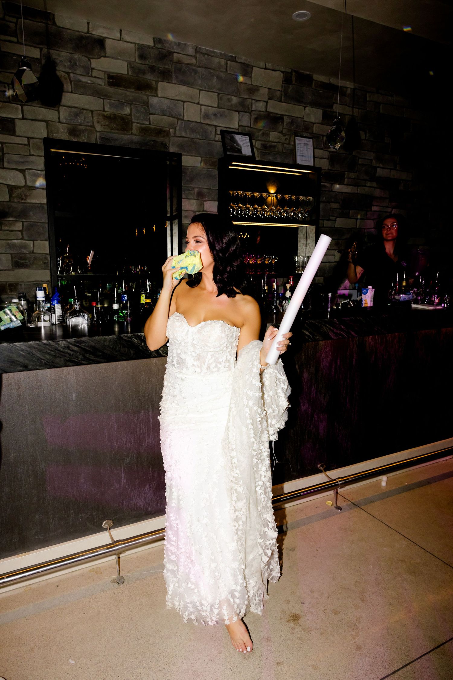 Wedding celebration at bar with person in white dress drinking and holding glowstick.