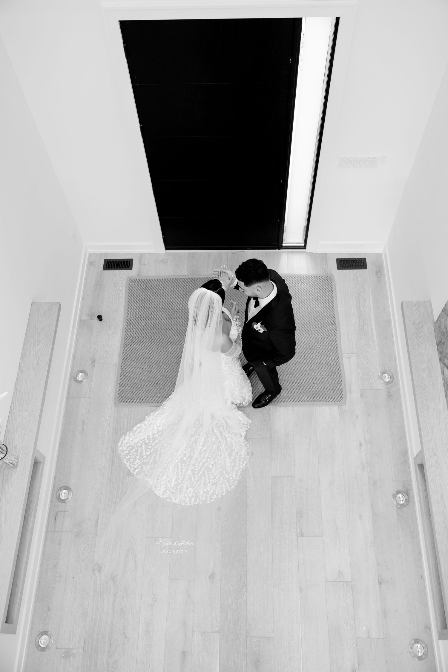 Overhead black and white view of a bride and groom standing on a light wooden floor.